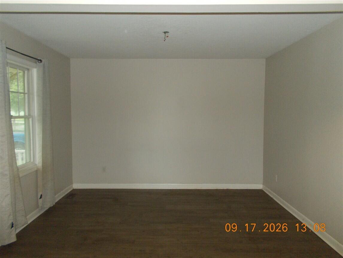 Empty room with dark wood flooring, gray walls, and a curtained window.