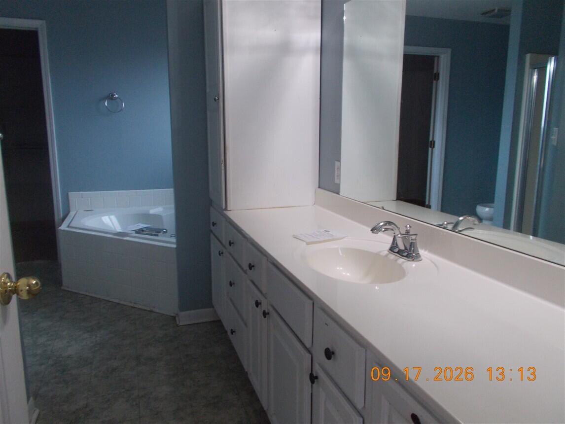 Bathroom with a long white vanity and a tiled soaking tub against blue walls.
