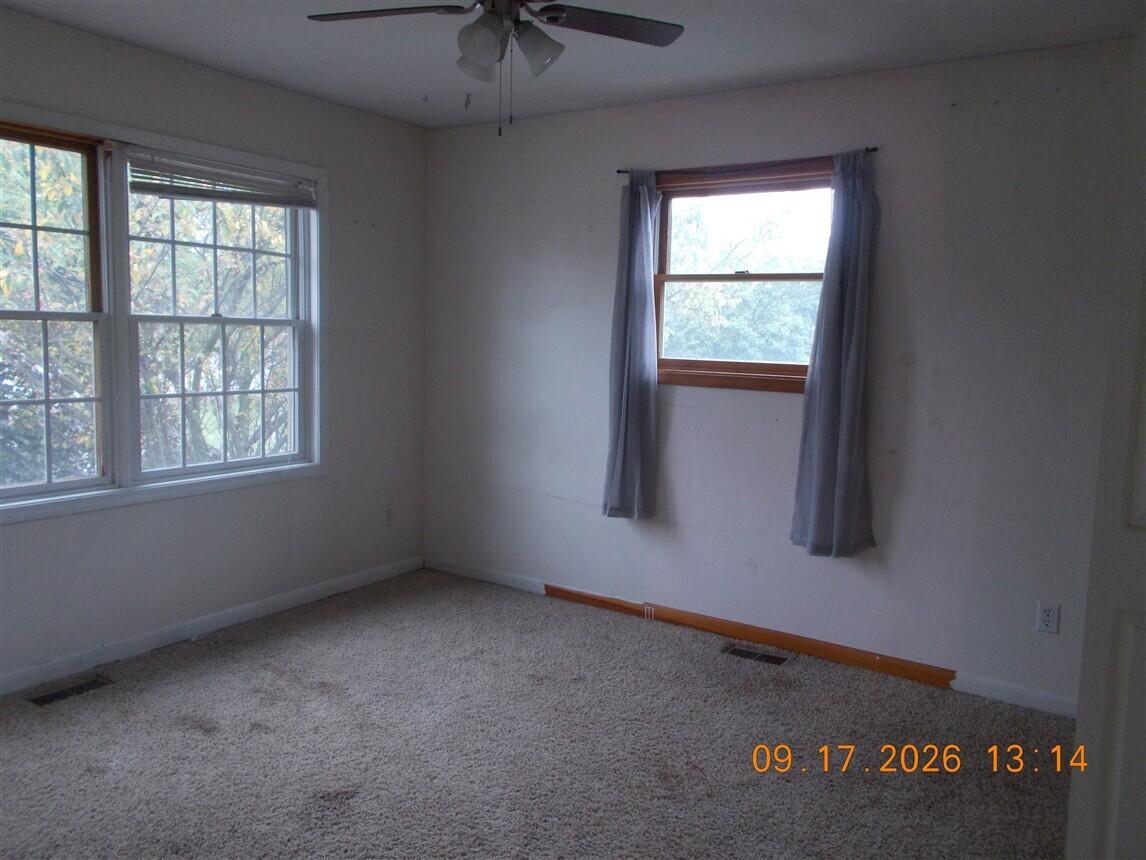 Empty carpeted bedroom with two windows and a ceiling fan.