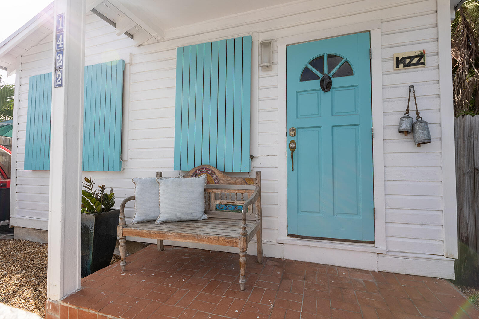 White house porch with turquoise door and shutters, a cushioned wooden bench, and the number 1422.