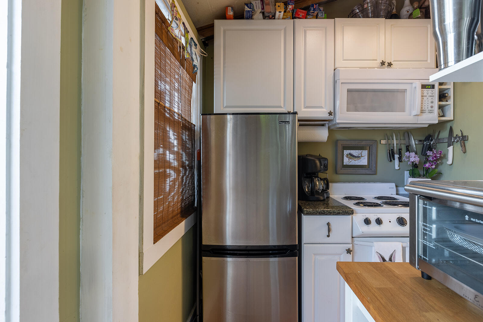 Compact kitchen with stainless-steel refrigerator, white cabinets, and a small electric range.