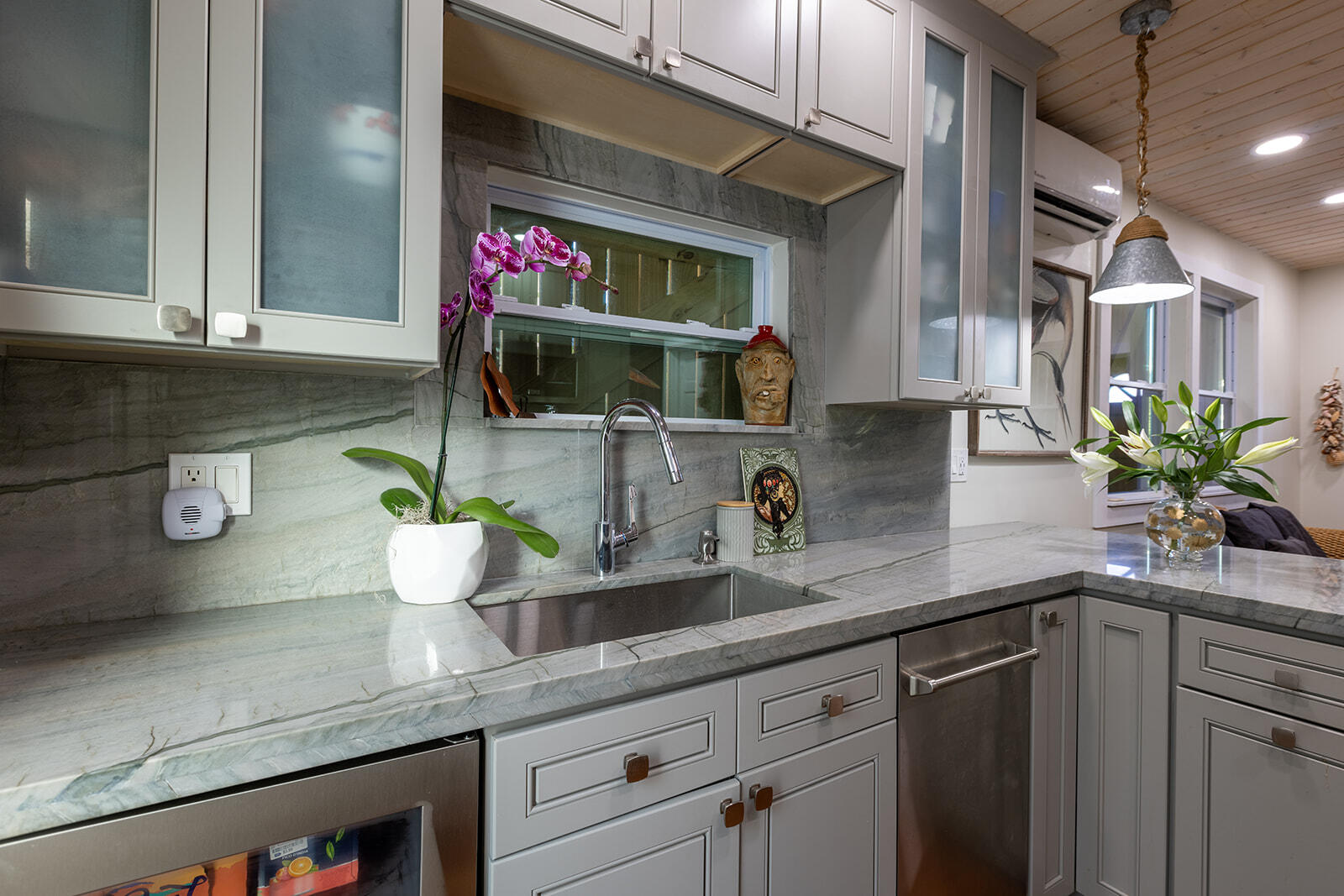 Kitchen with veined marble counters, white cabinets, stainless steel appliances, and orchids.
