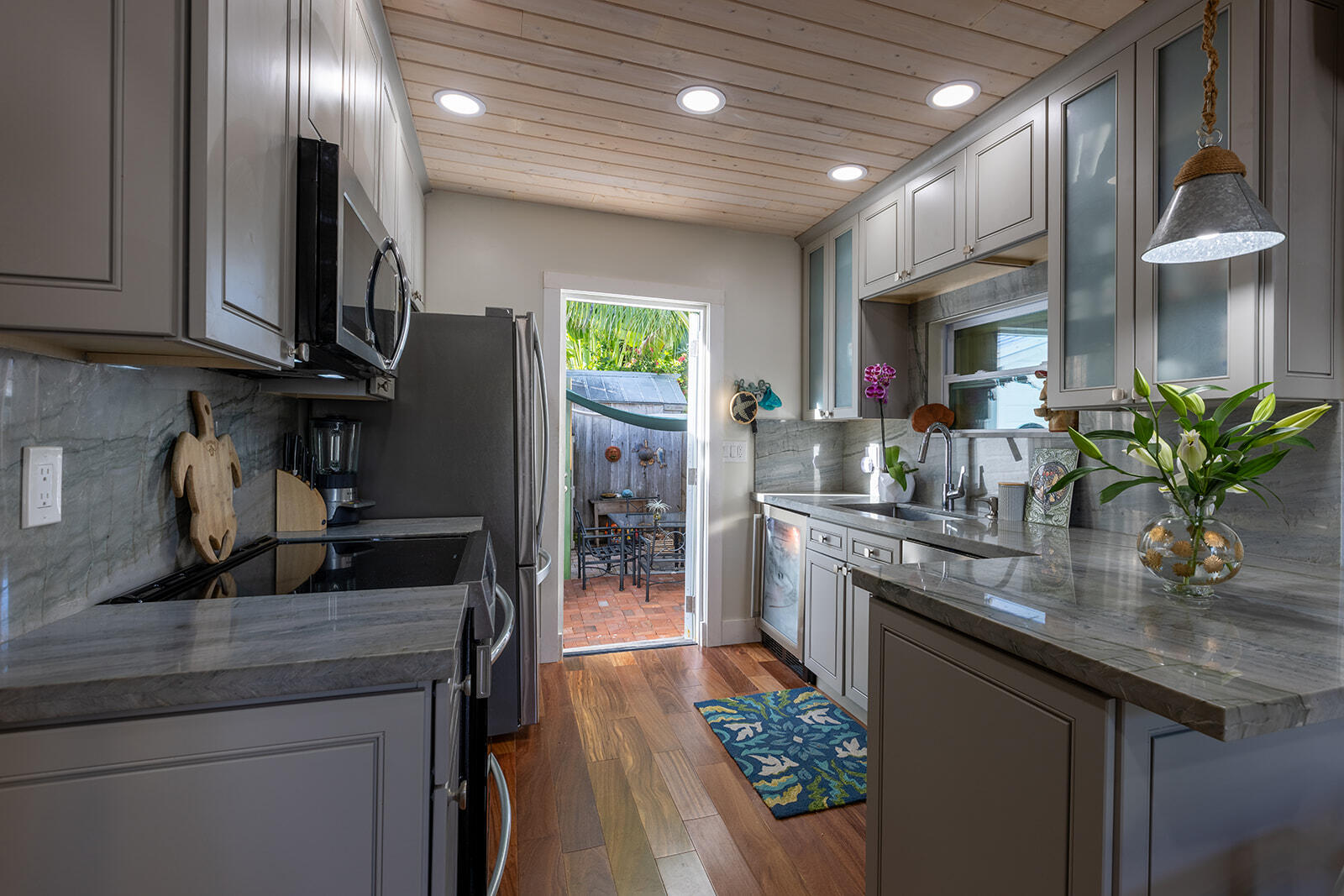 Kitchen with gray cabinets and marble counters, opening onto a small brick patio.