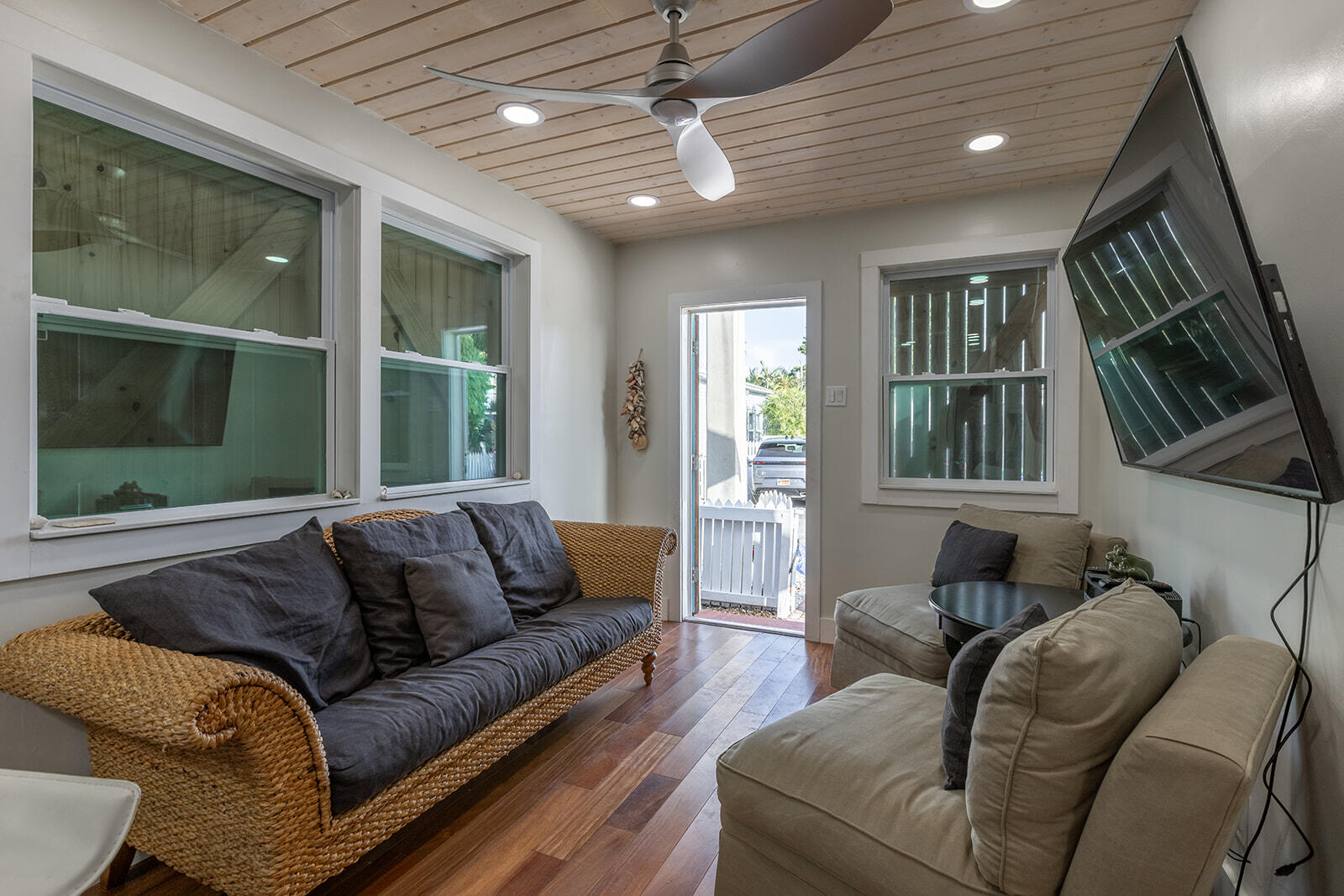 Living room with wicker sofa, beige sectional, wood floors, and a plank ceiling.