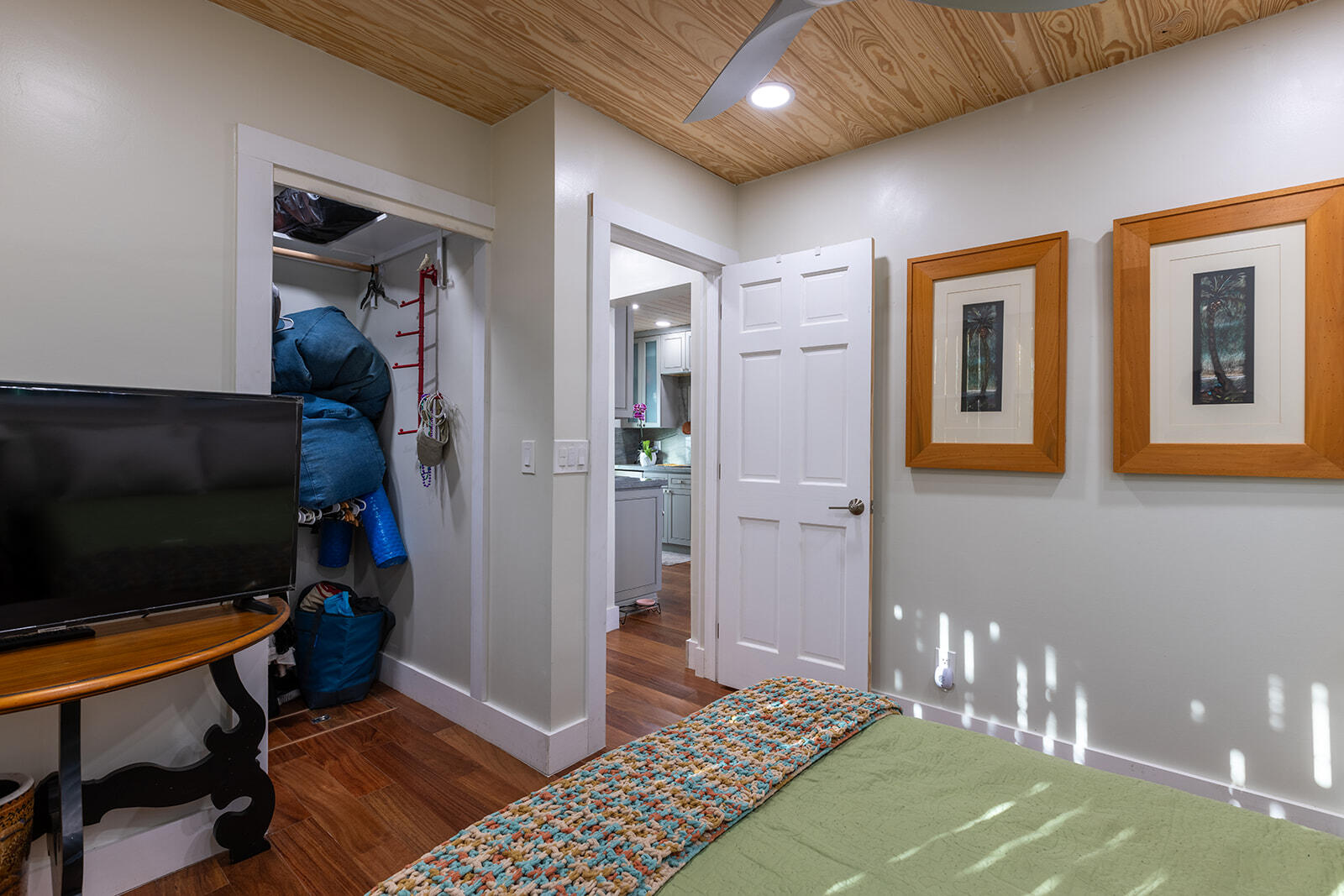 Bedroom with a green bedspread, colorful runner, plywood ceiling, and open closet.