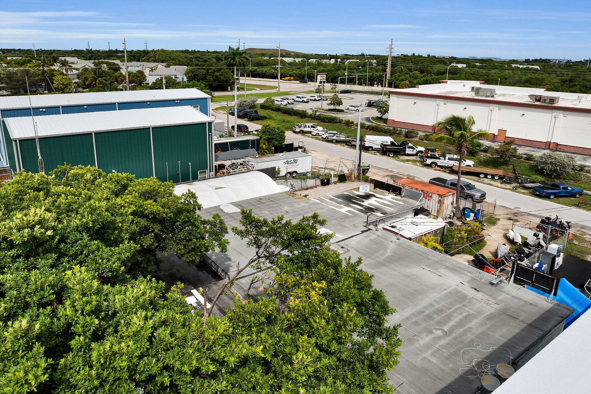 Aerial view of a commercial property with flat roofs, fenced work areas, and tropical greenery.