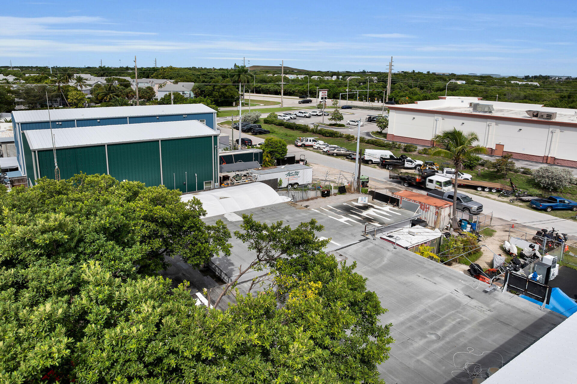 Commercial property with broad rooftops and paved work areas, viewed from above amid tropical greenery.