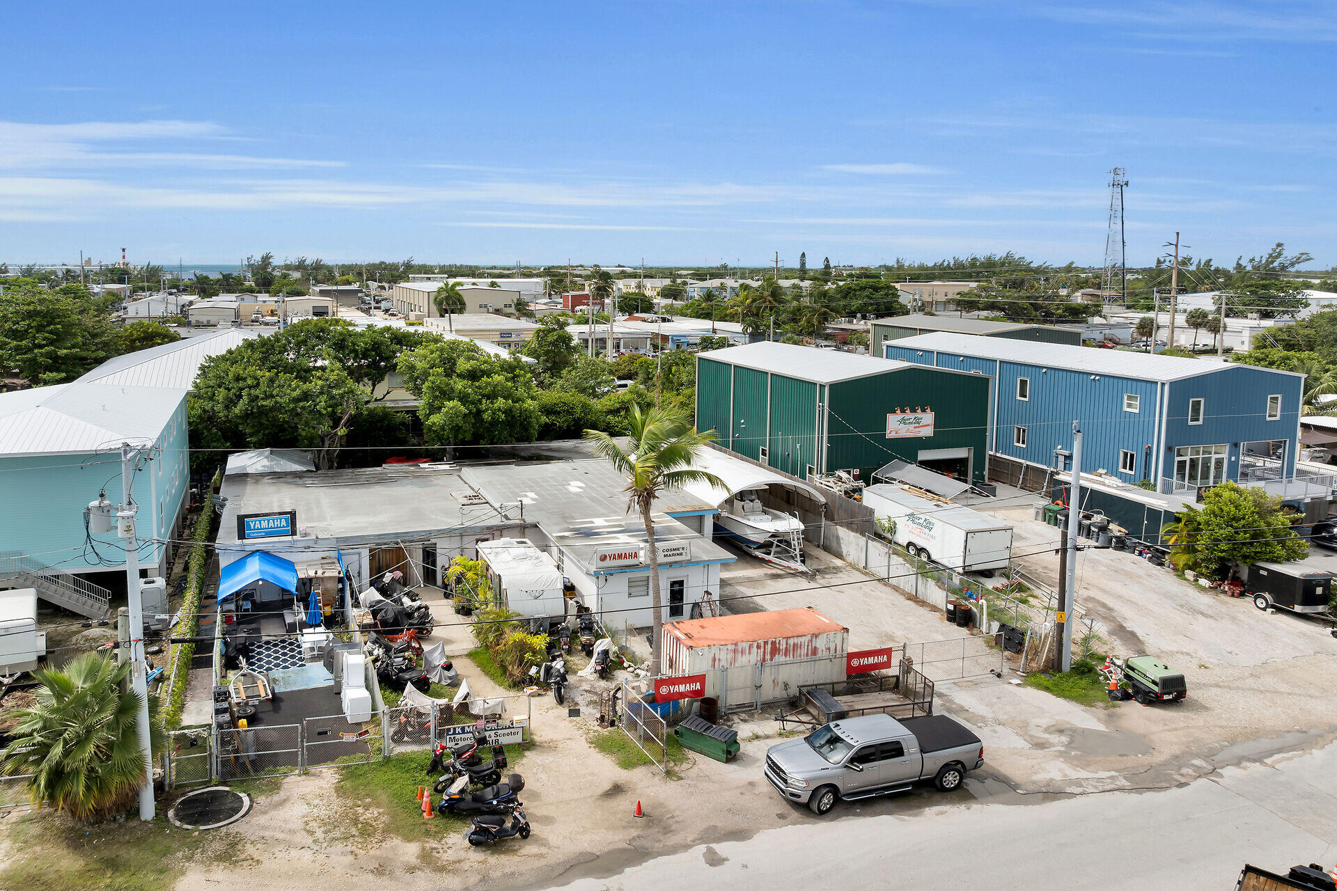 Elevated view of marine businesses and boat storage, with blue and green buildings and ocean on the horizon.