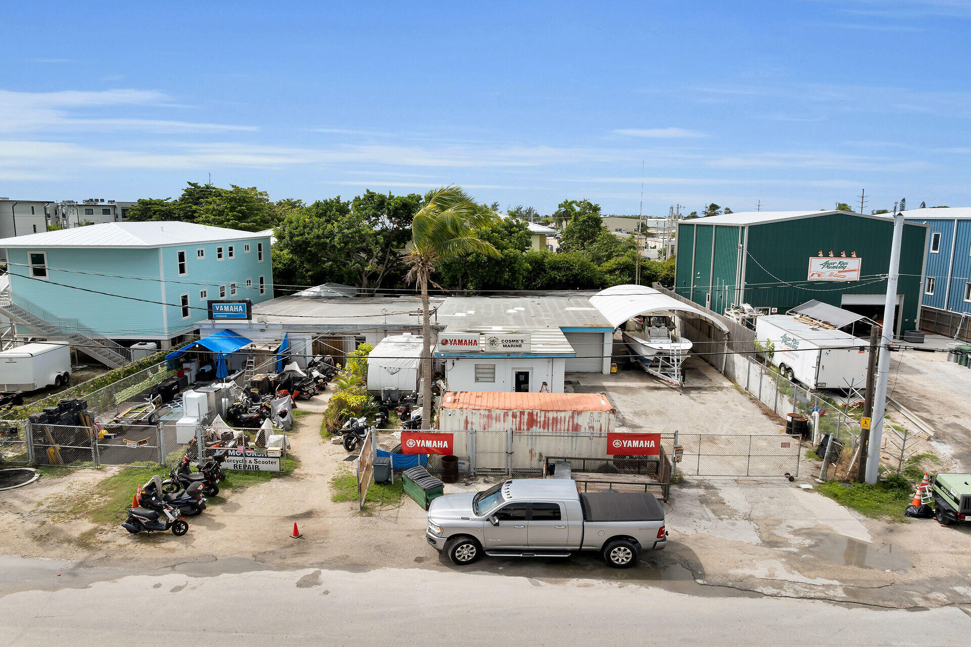 Aerial view of a marine service yard with a covered boat, Yamaha signs, scooters, and industrial buildings.