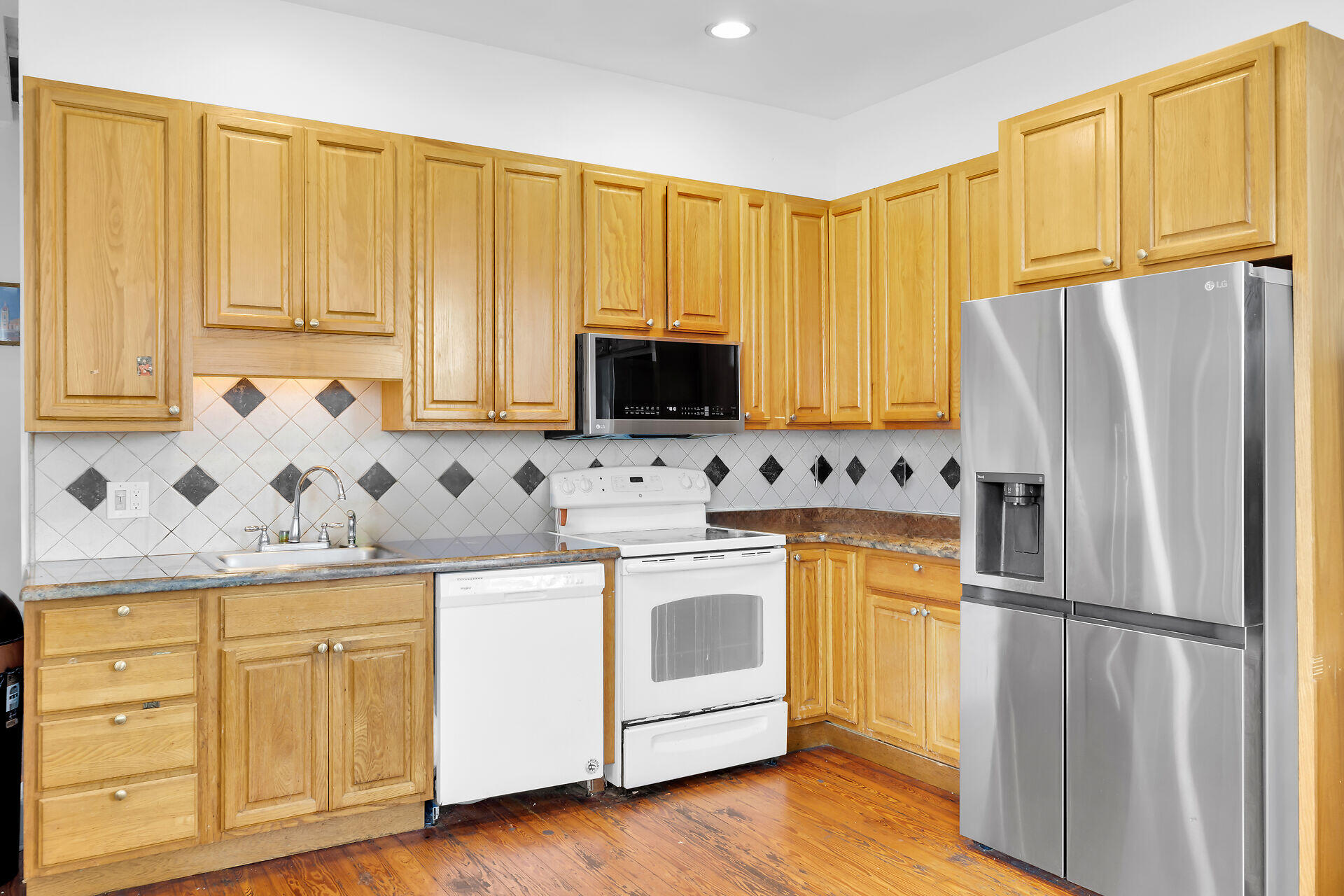 Kitchen with honey-colored wood cabinets, a diamond-pattern tile backsplash, and a stainless-steel refrigerator.