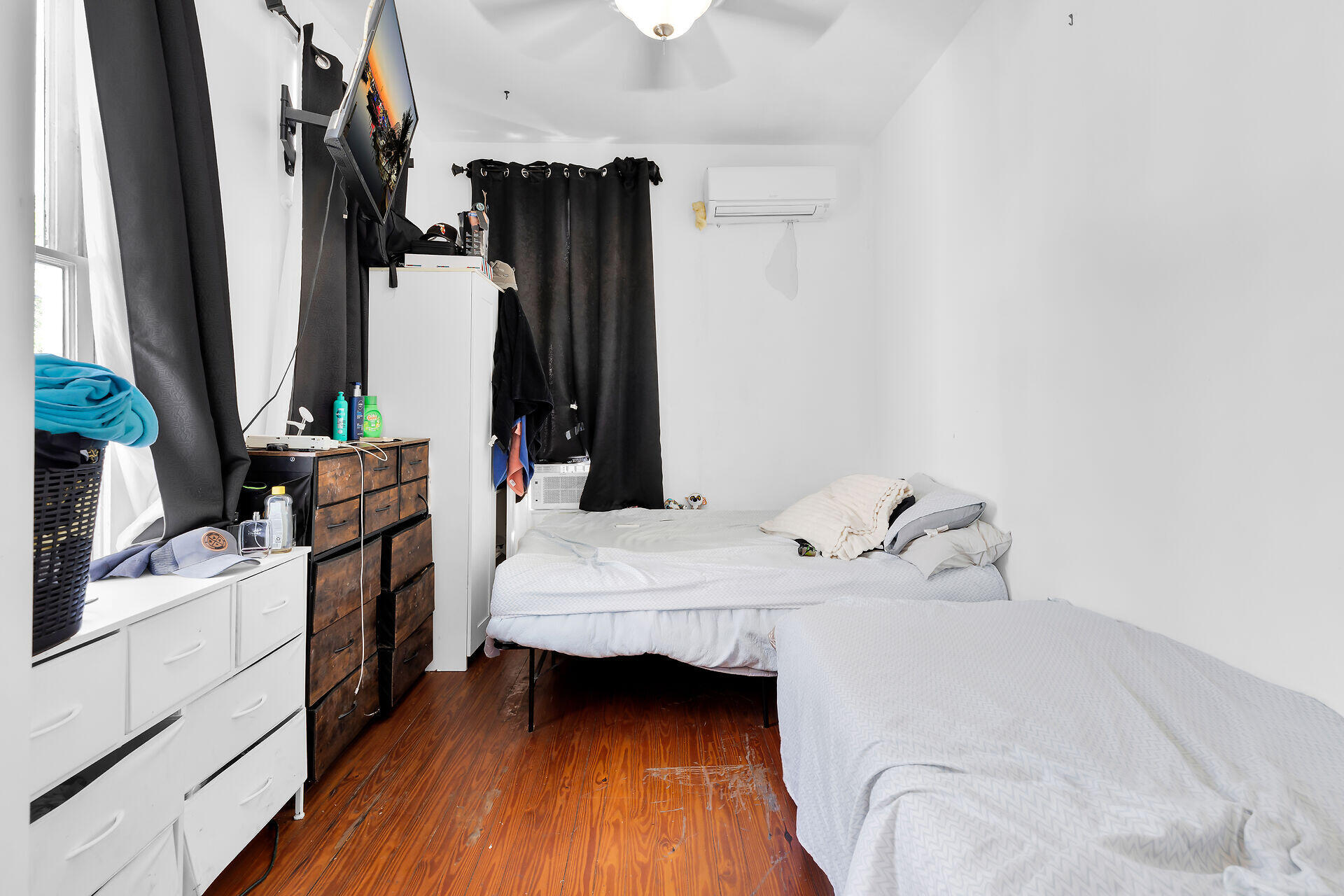 Bedroom with two beds, dark curtains, wood floors, and a wall-mounted television.