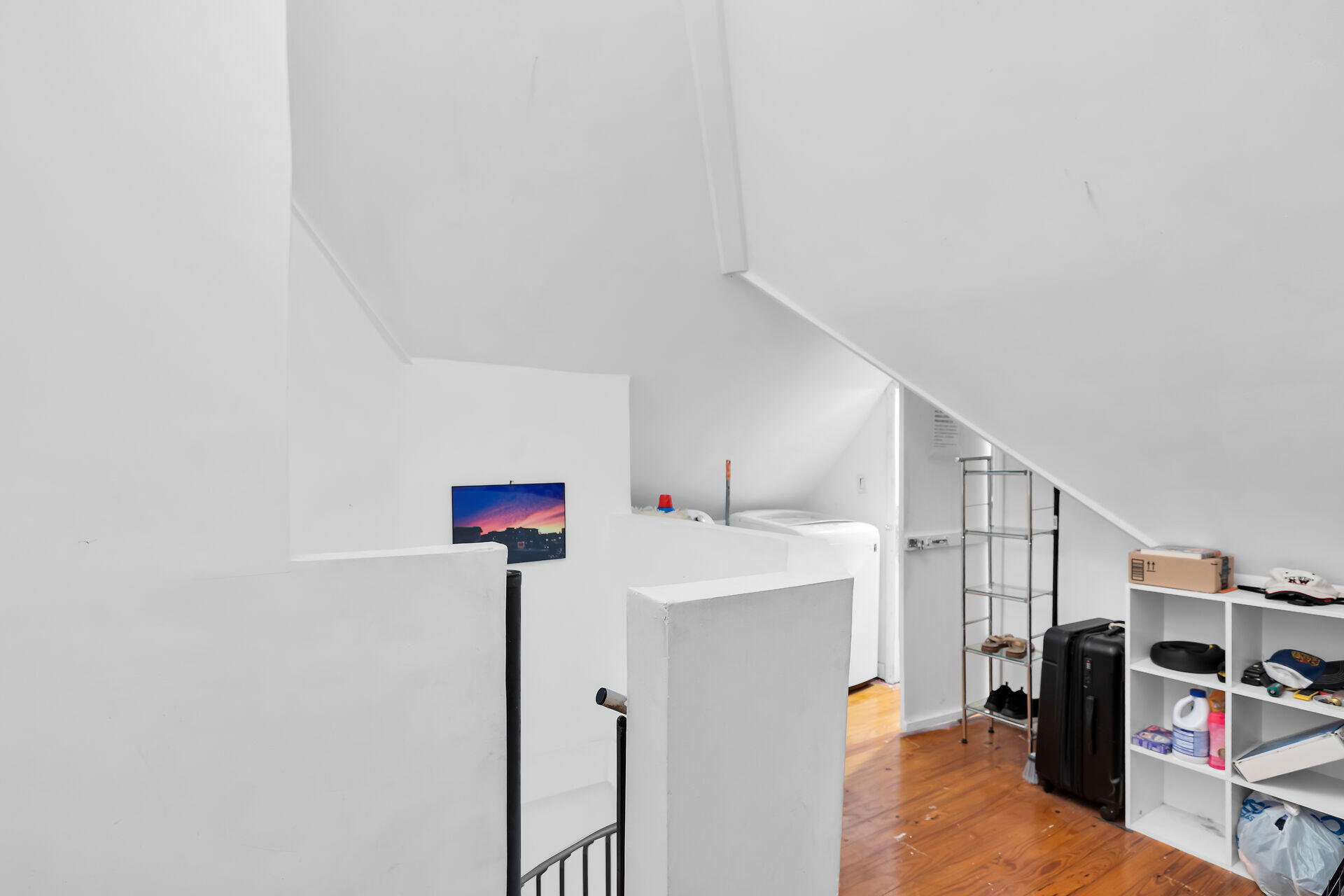 Upper-level bedroom with a sloped ceiling, low white partitions, hardwood floor, and open storage shelves.