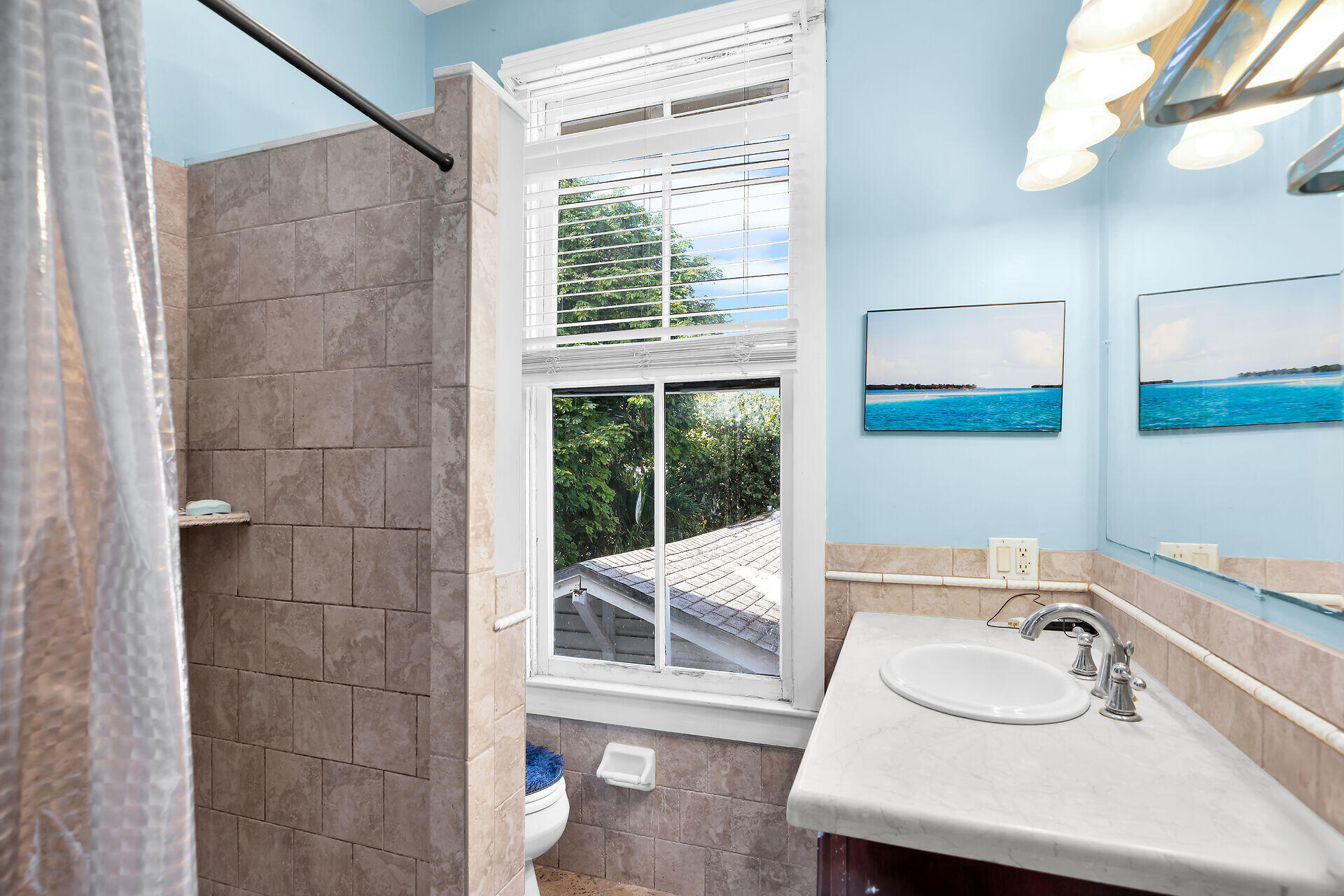 Bathroom with a tiled shower, white vanity, and window with blinds.