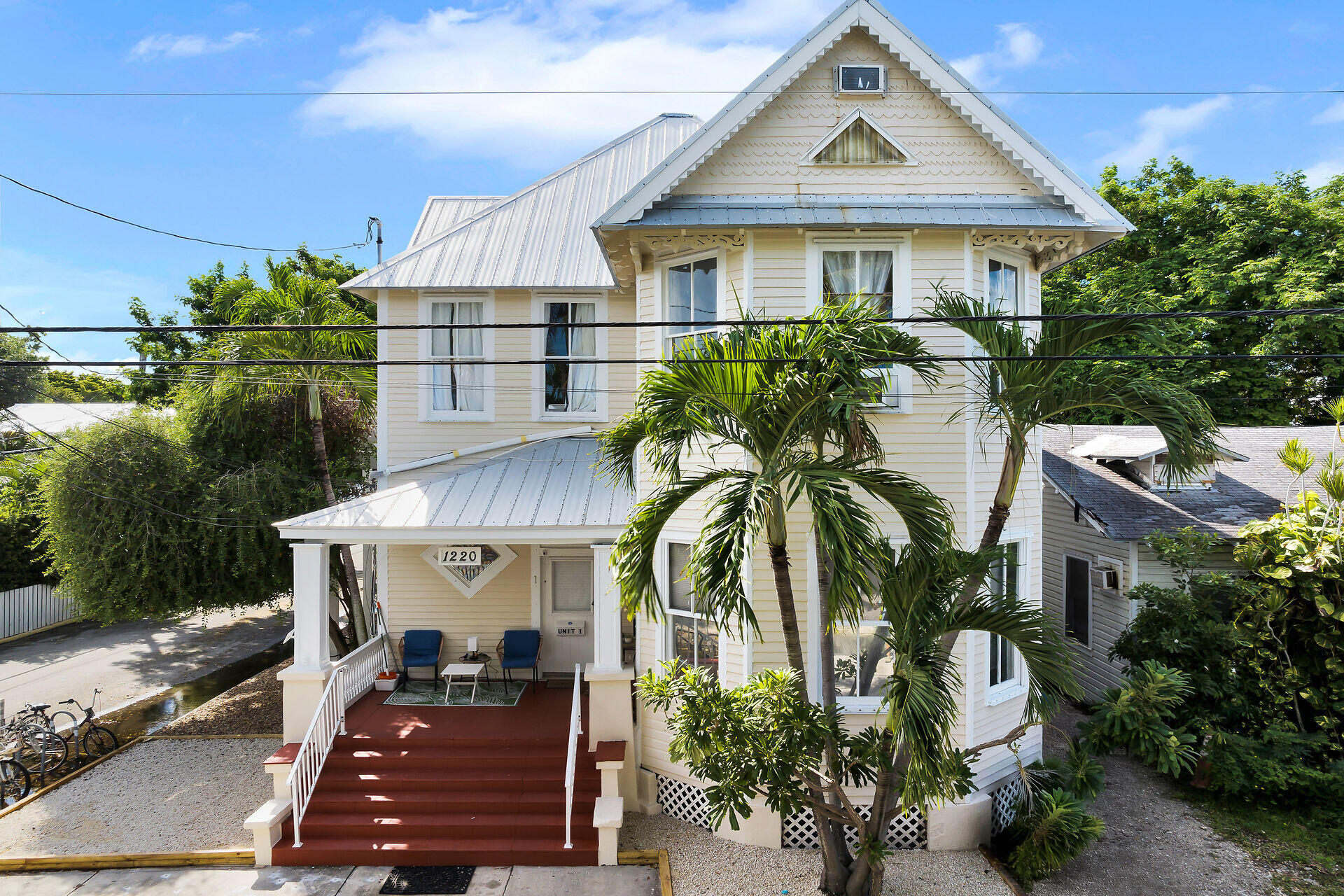 Cream two-story house with a steep gabled roof, palm trees, and a red front porch.