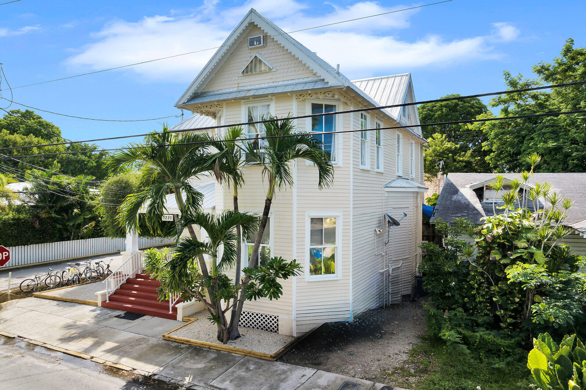 Cream two-story house with a steep gabled metal roof, palm trees, and red front steps.