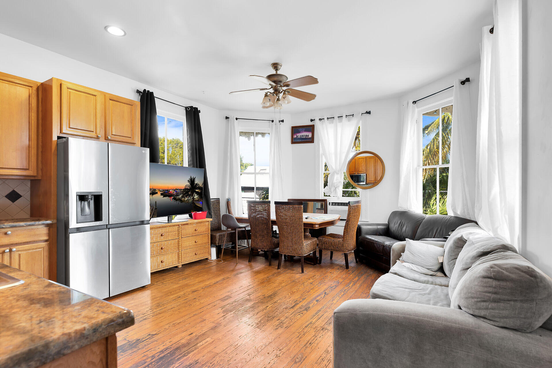 Open-plan kitchen and living room with wood floors, wicker dining chairs, and gray sofas.