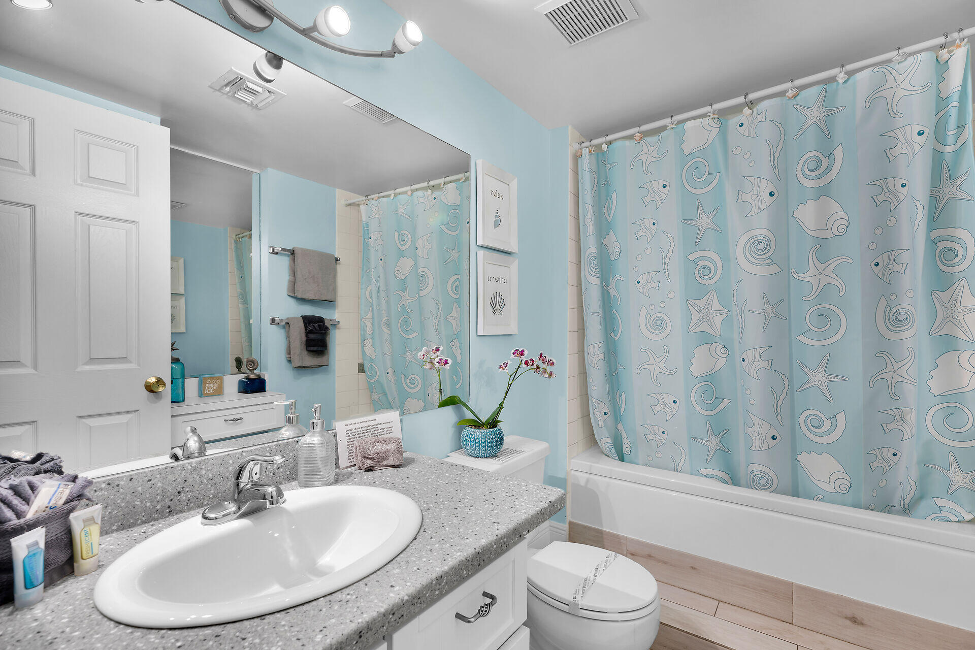Bathroom with a speckled vanity, pale blue walls, and a sea-life patterned shower curtain.