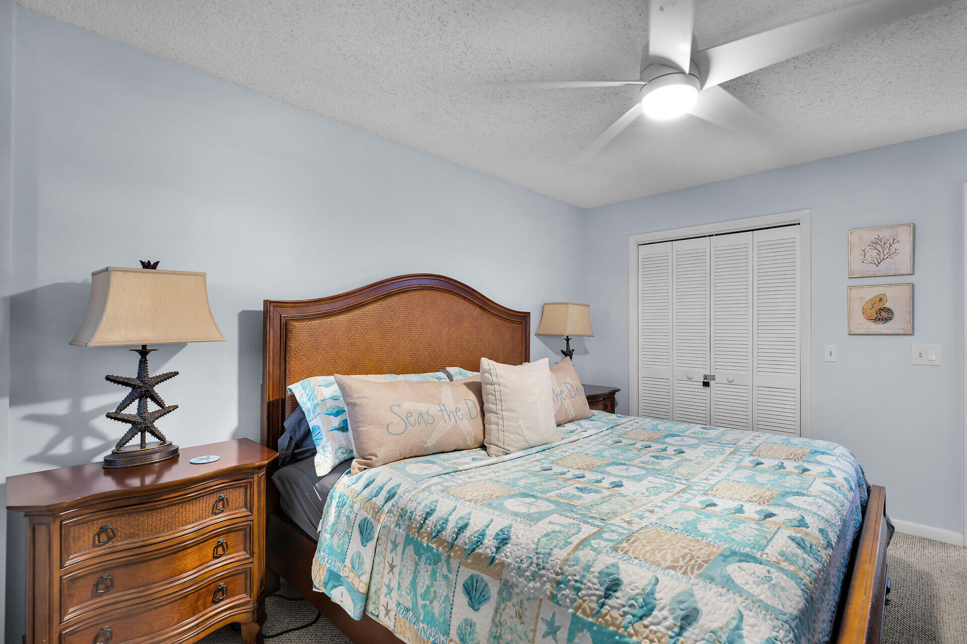 Furnished bedroom with a wooden bed, coastal-patterned bedding, and pale blue walls.