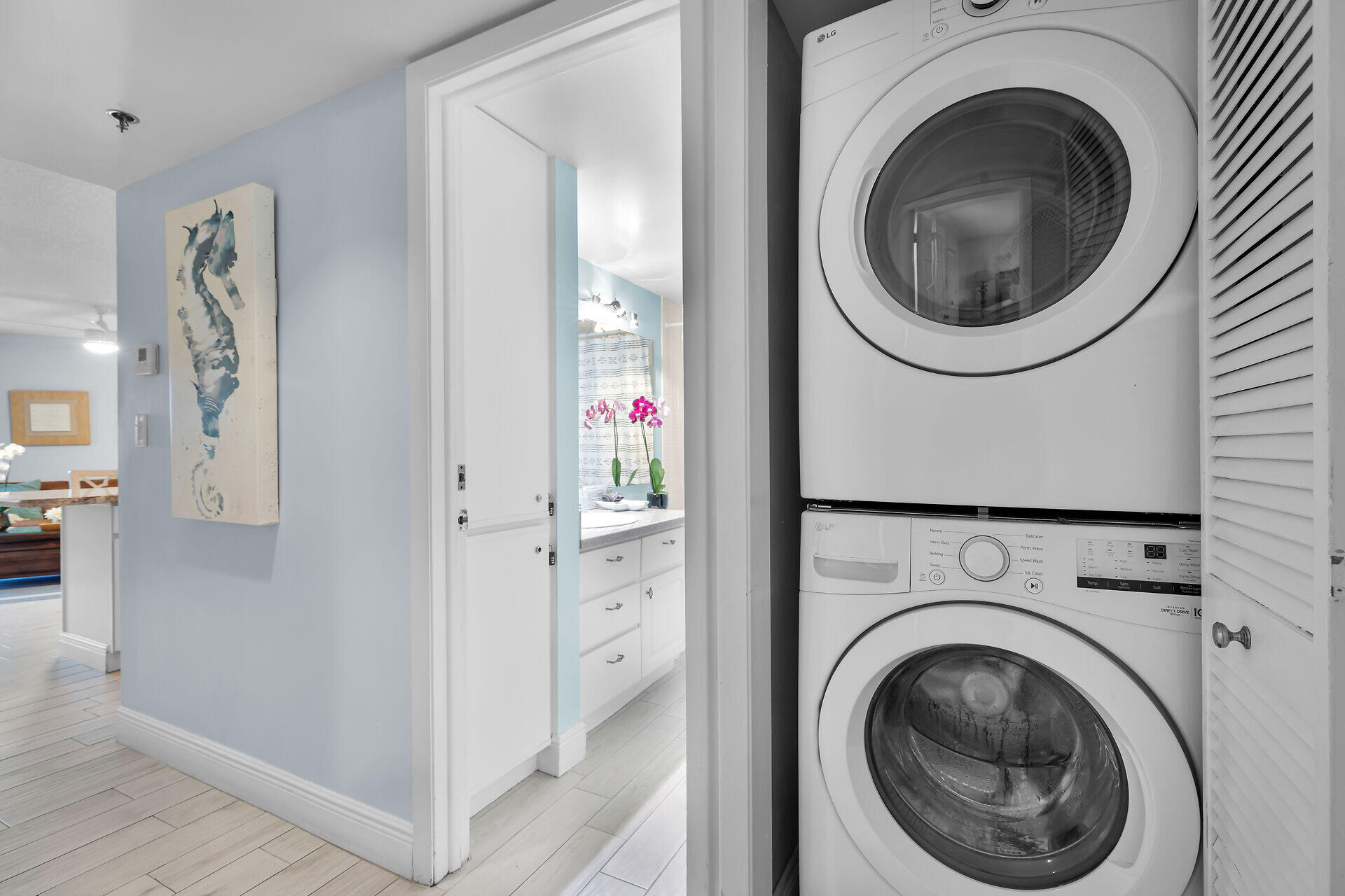 Stacked white washer and dryer in a closet beside a bathroom with pink orchids.