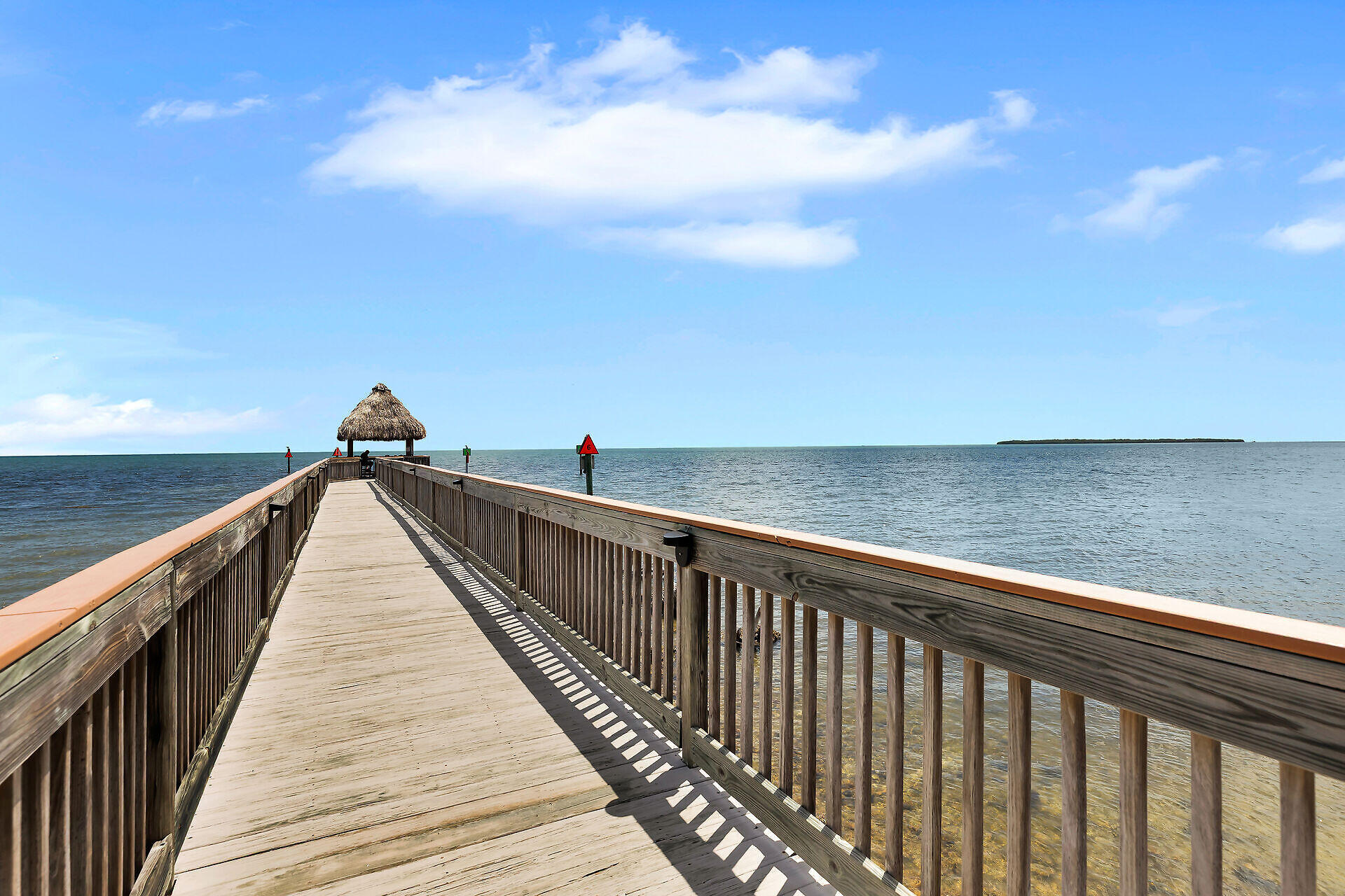 Wooden pier with a thatched-roof shelter extending over calm ocean water.