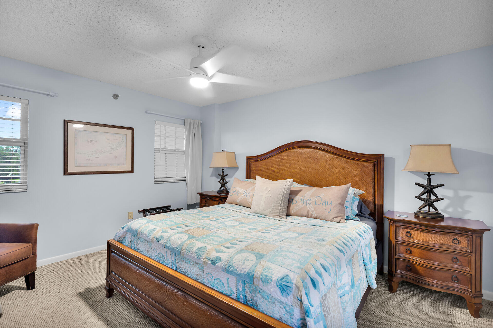 Bedroom with a woven wooden headboard, blue coastal bedding, matching furniture, and a lit ceiling fan.