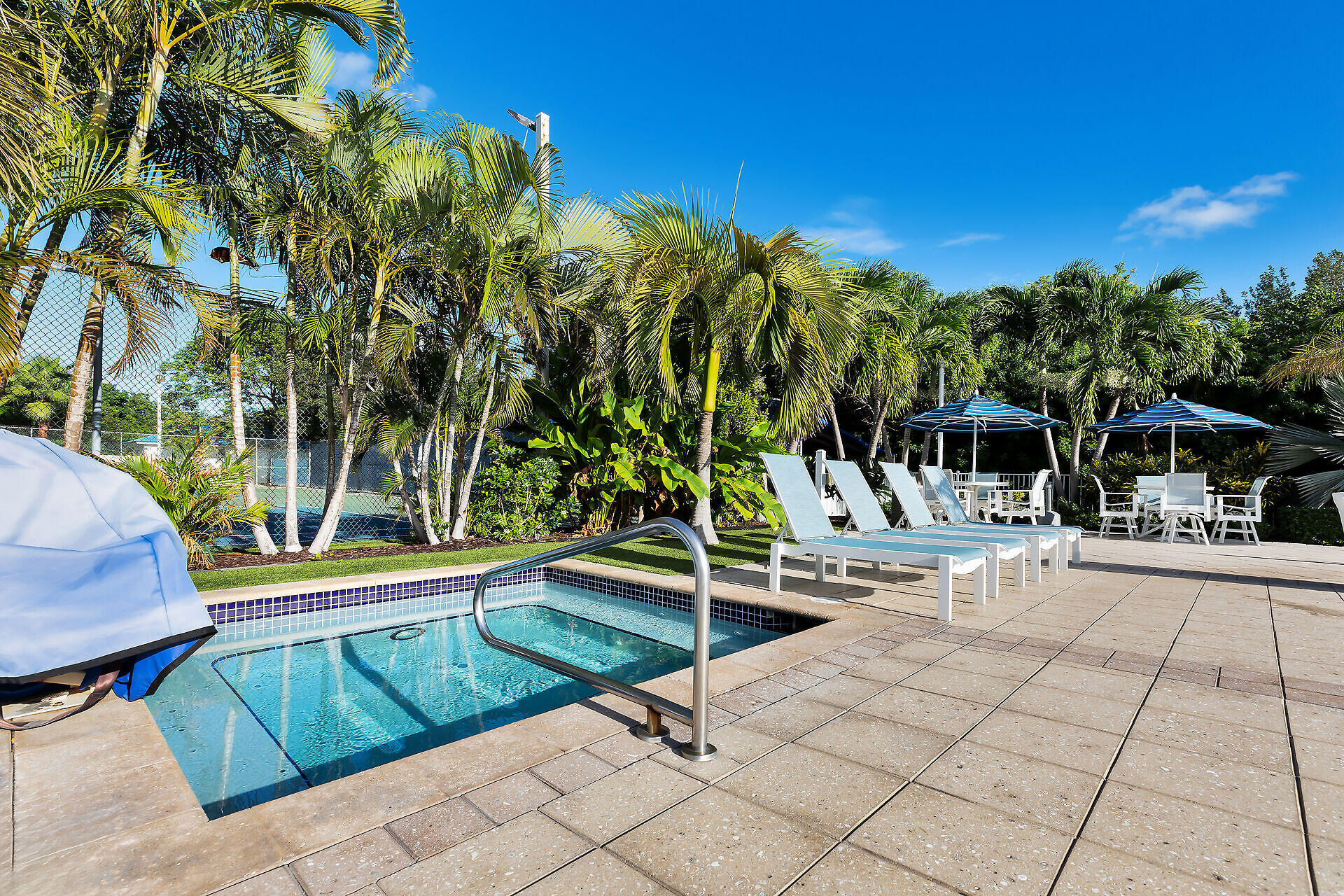 Outdoor pool with white loungers and umbrellas, surrounded by palm trees.
