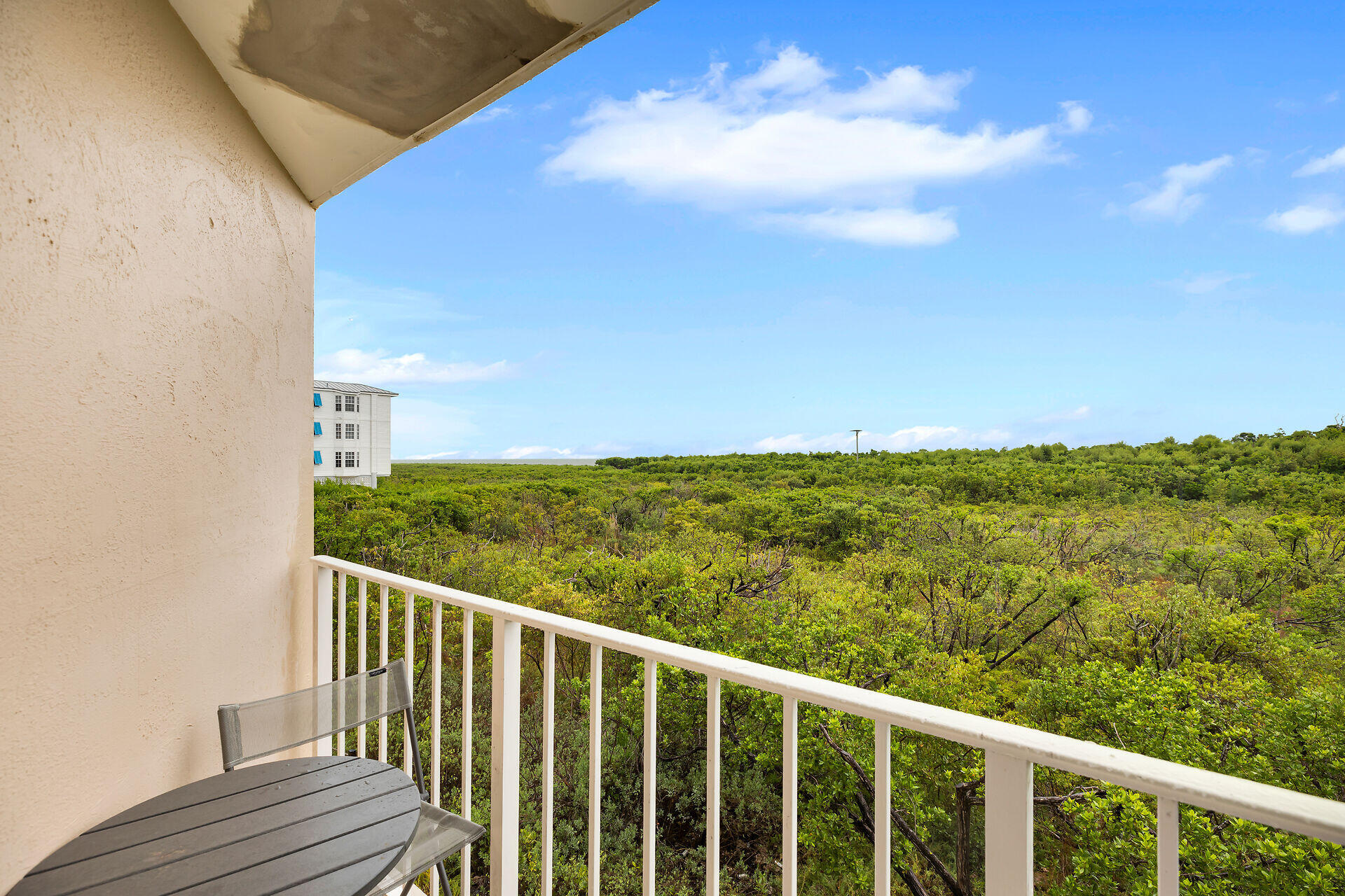 Condo balcony overlooking dense green vegetation, with a white railing and round patio table.