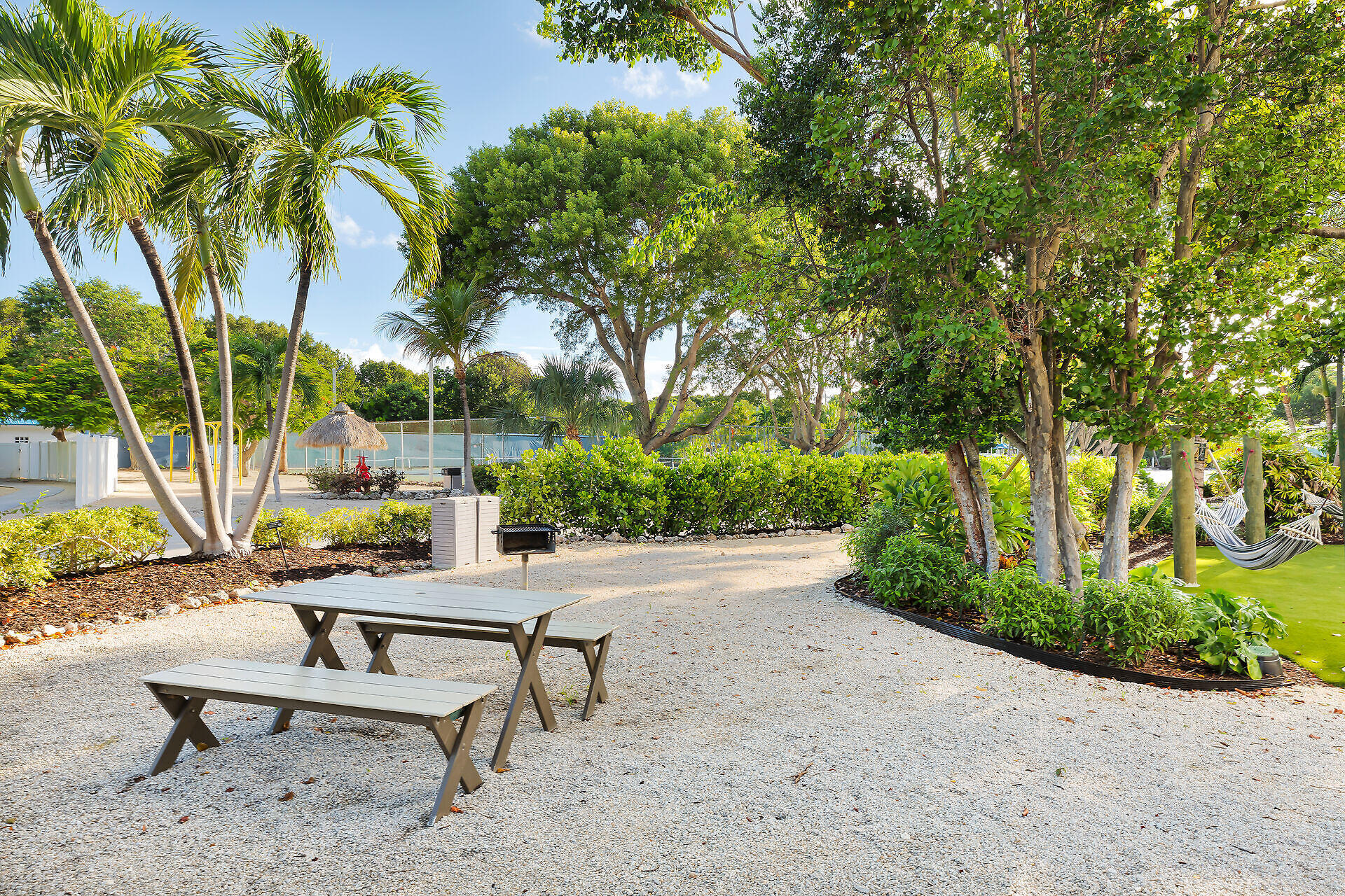 Outdoor recreation area with picnic tables, palm trees, hammocks, and a fenced court.