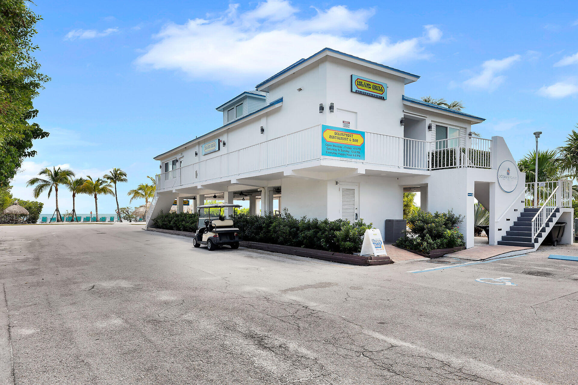 White Ocean Pointe restaurant building with a balcony, exterior stairs, golf cart, palm trees, and ocean view.