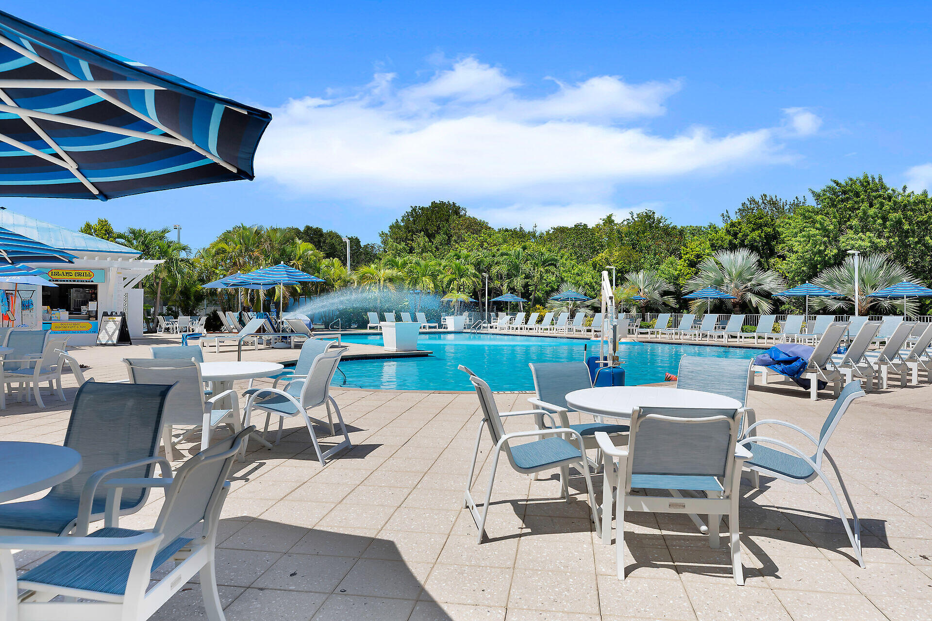 Outdoor swimming pool with blue-striped umbrellas, lounge chairs, and a poolside grill.