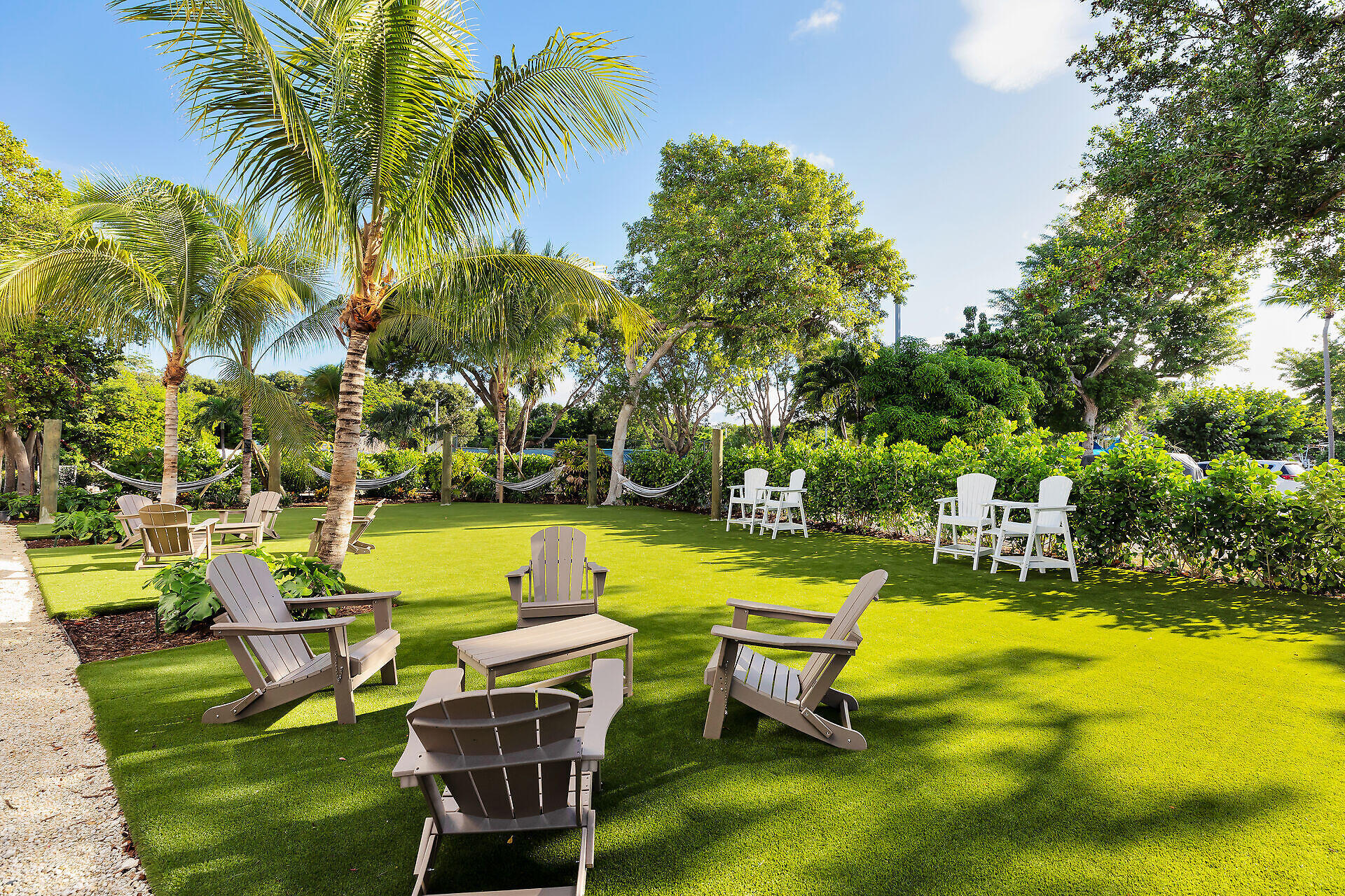 Outdoor seating area with Adirondack chairs, hammocks, artificial turf, and tropical palms.