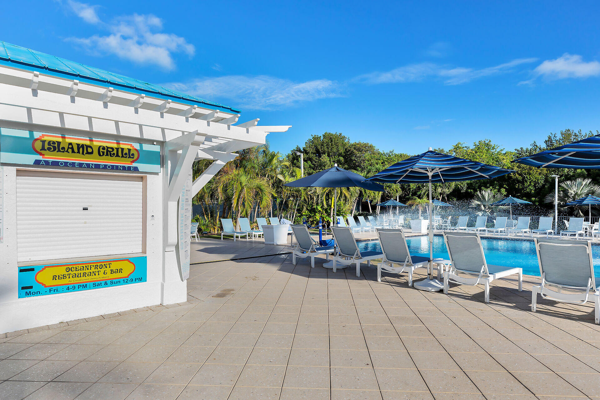 Ocean Pointe pool with blue umbrellas, lounge chairs, and an Island Grill kiosk.