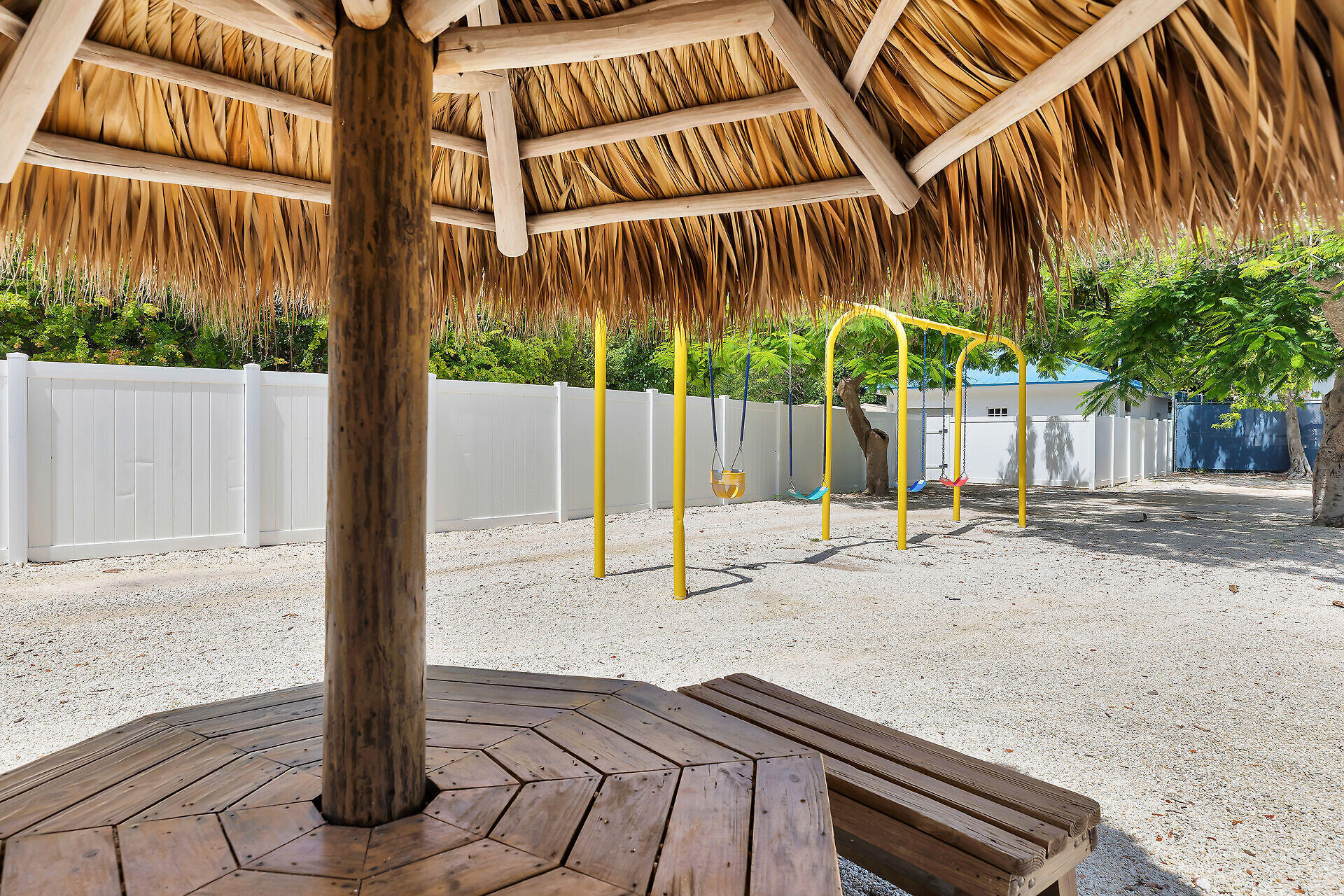 Outdoor playground with colorful swings beneath a thatched tiki pavilion.