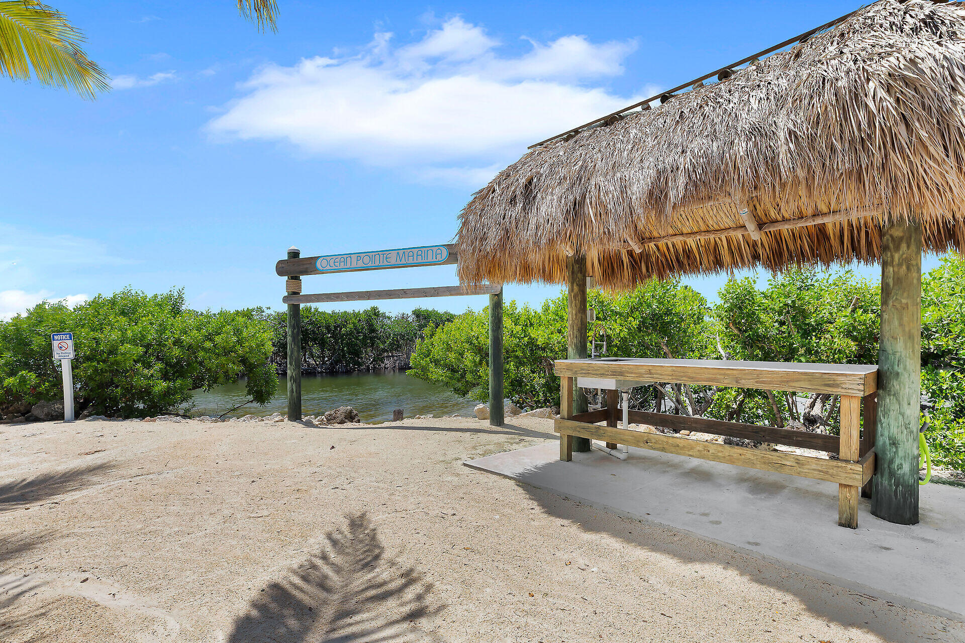 Marina entrance with an Ocean Pointe Marina sign, mangroves, and a thatched-roof shelter.