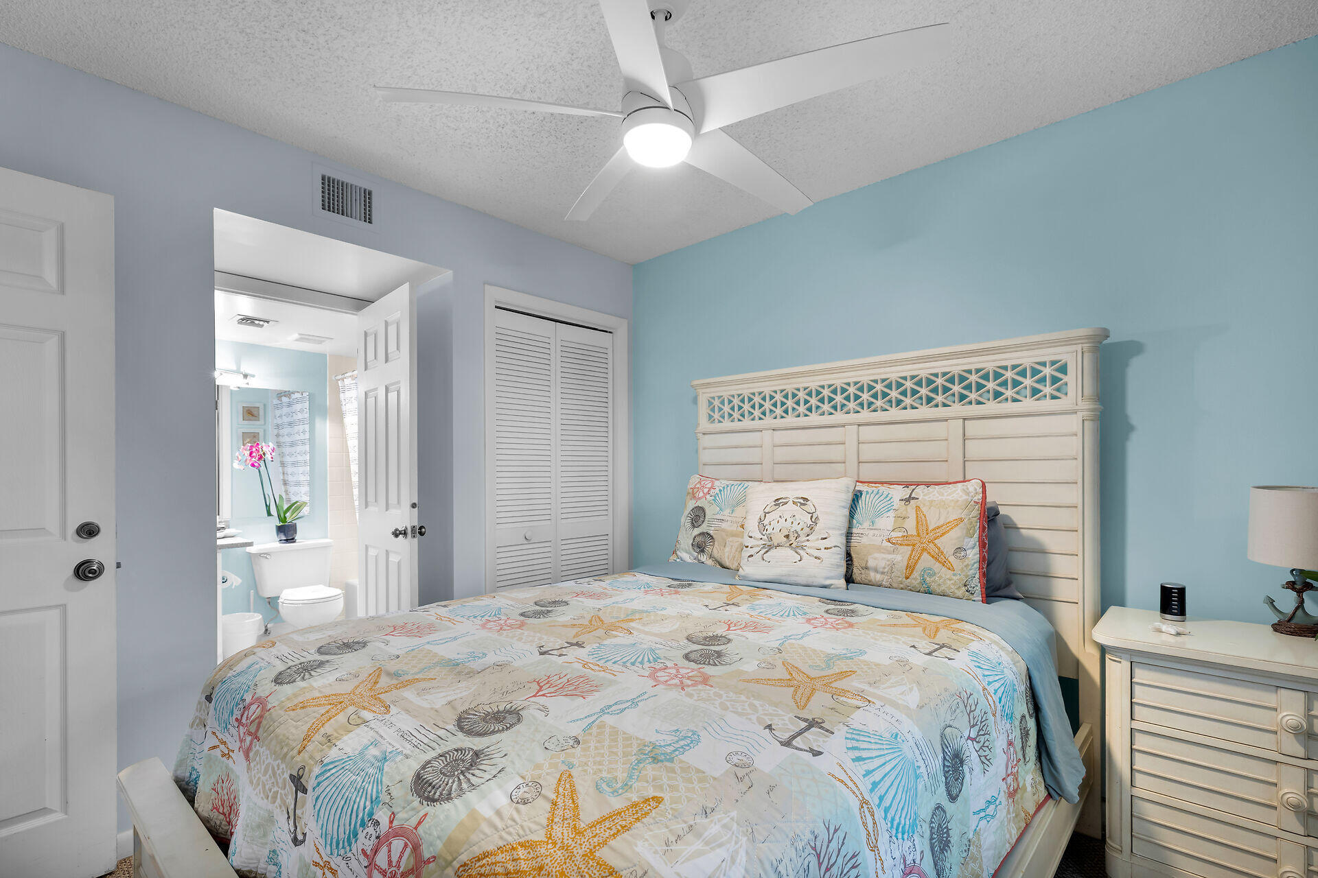 Bedroom with seashell-patterned bedding, a white headboard, and an open doorway to the bathroom.