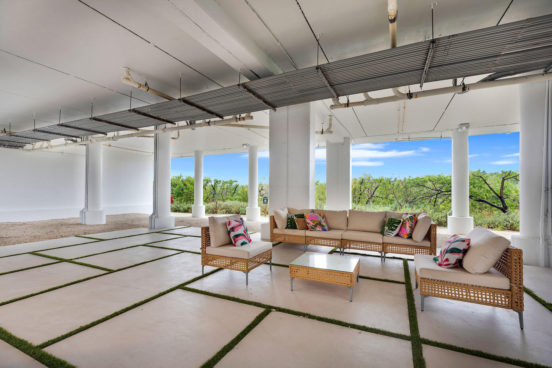 Covered patio with wicker lounge seating, grass-lined pavers, and views of green vegetation.