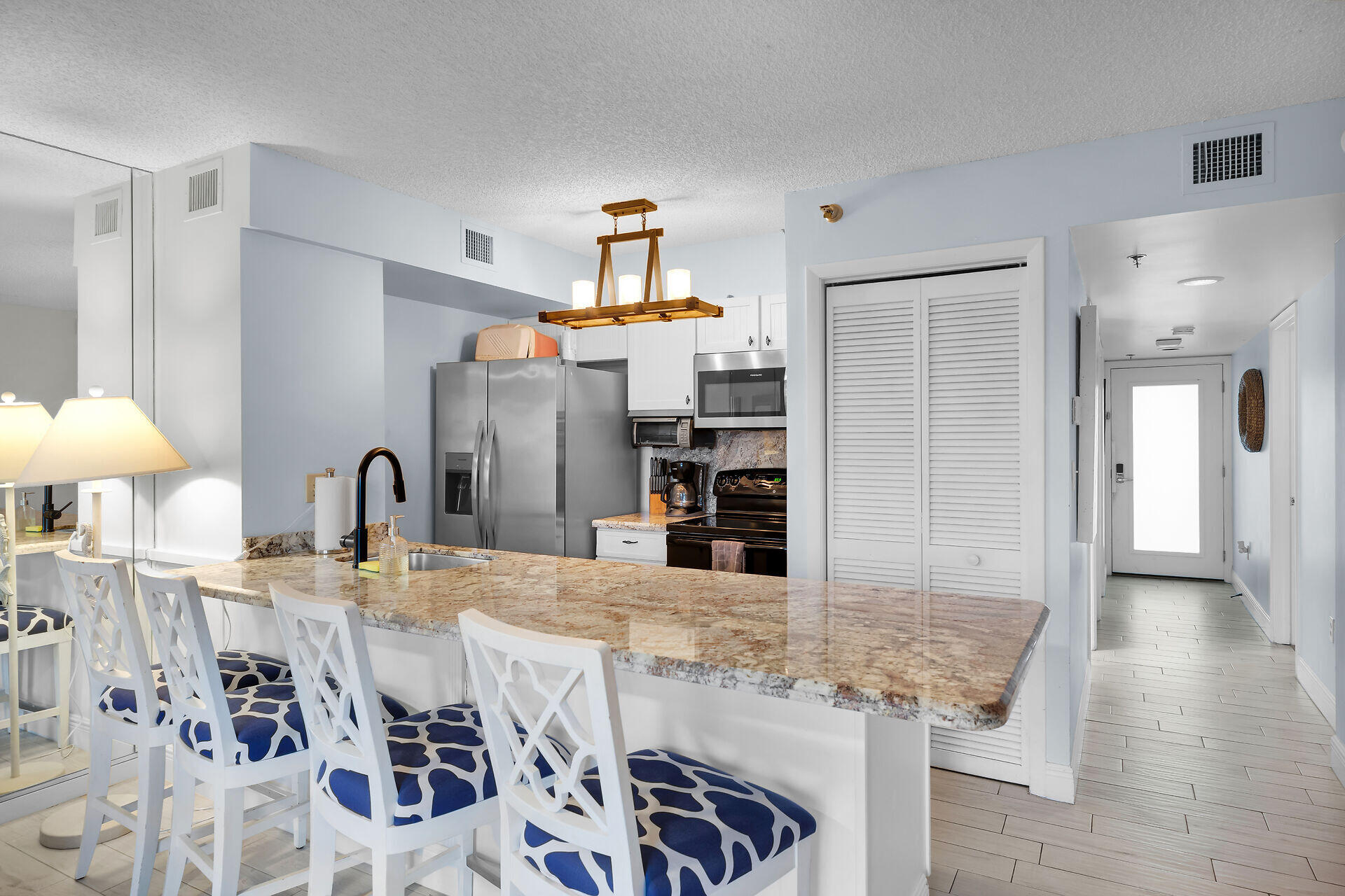 Condo kitchen with a granite breakfast bar, patterned stools, and stainless steel appliances.