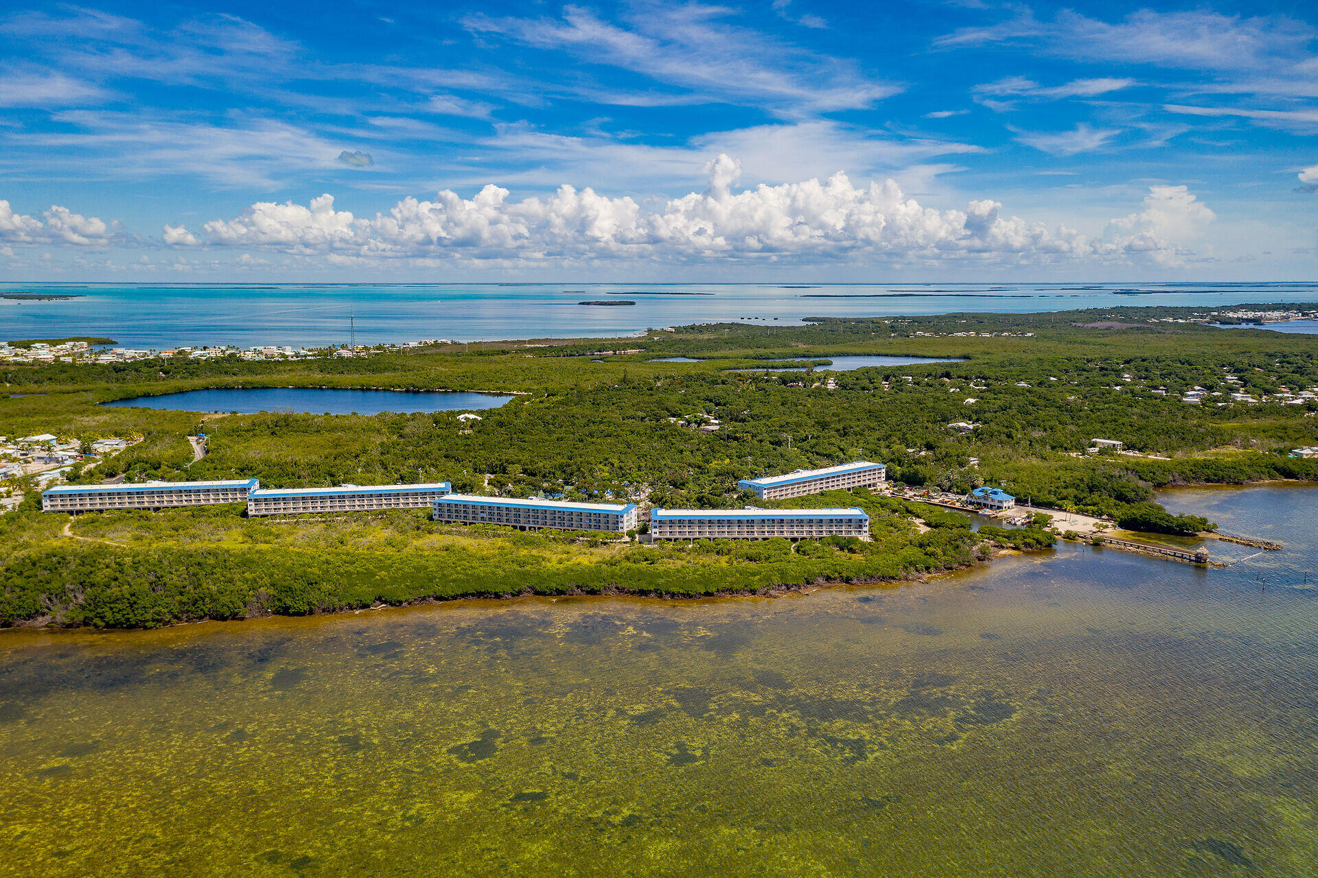 Aerial view of waterfront condominium buildings along a mangrove shoreline, with shallow bay waters and islands beyond.