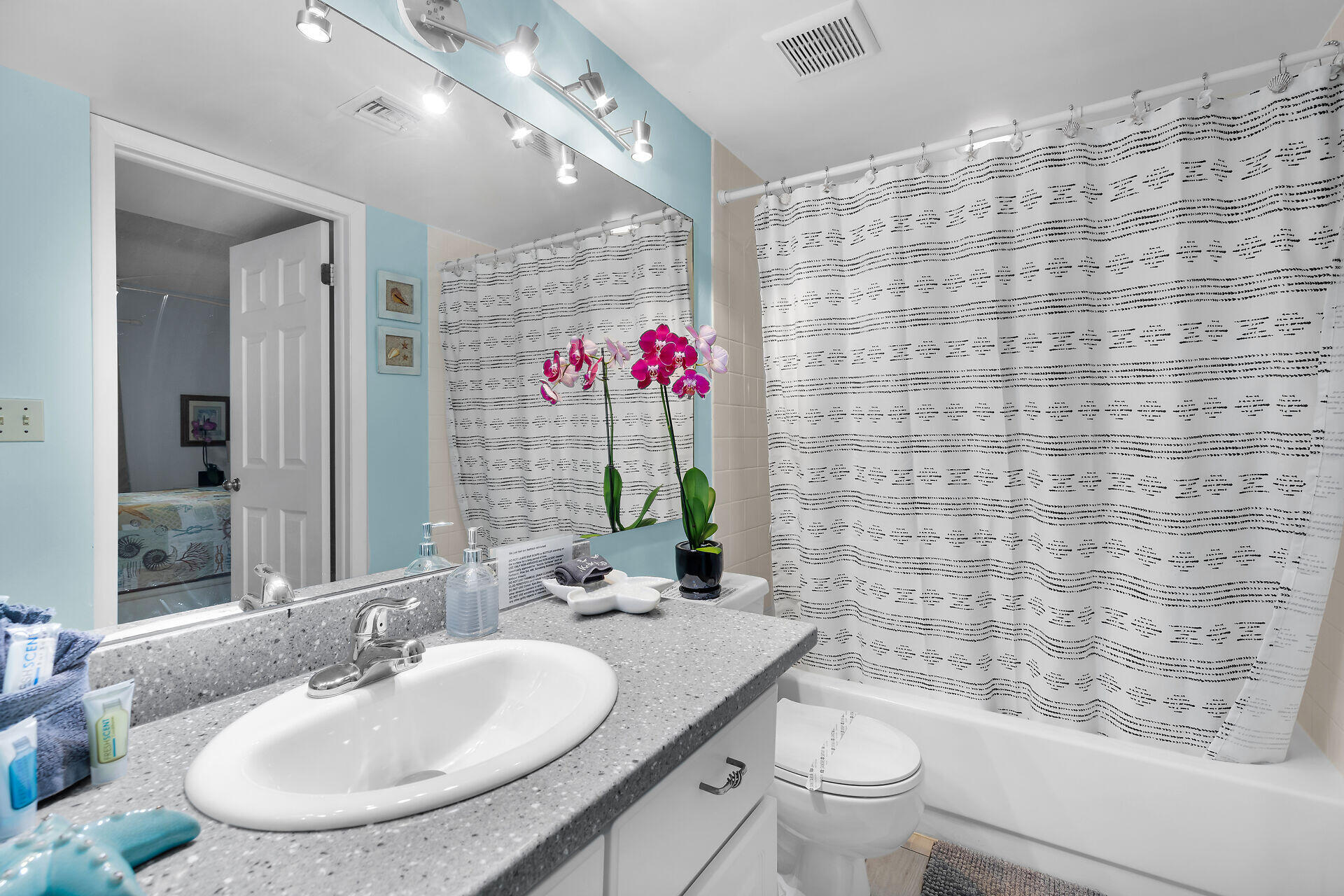 Bathroom with a gray vanity, pink orchids, and a bathtub behind a patterned shower curtain.