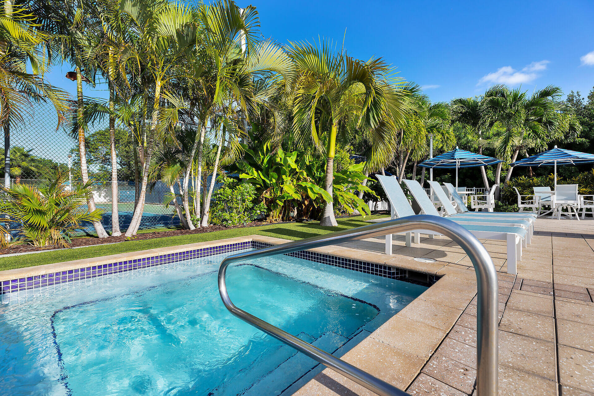 Outdoor pool with tropical palms, white loungers, and blue shade umbrellas.