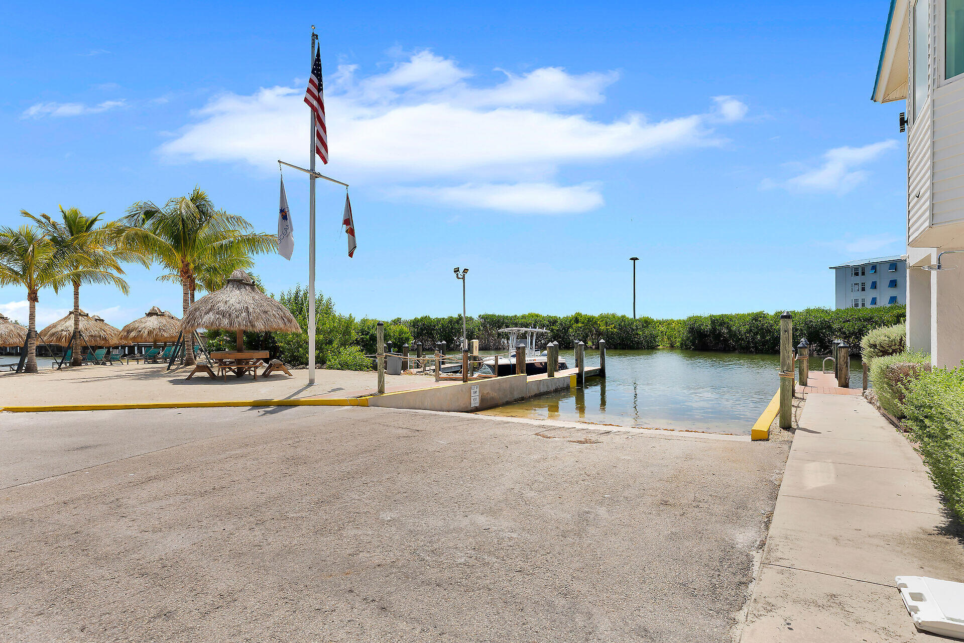 Waterfront dock beside a calm canal, with palm trees and thatched shade huts.