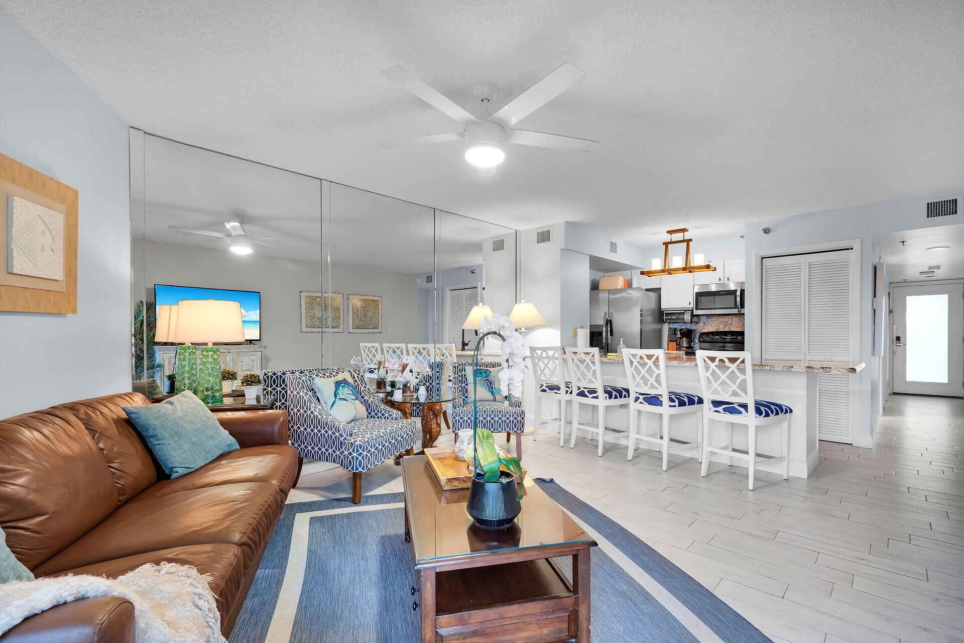 Open-plan living room and kitchen with a leather sofa, mirrored wall, and island bar seating.