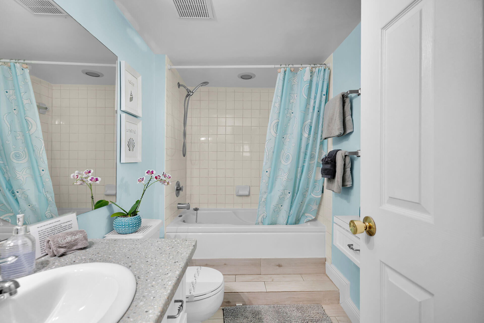 Bathroom with a tub and tiled shower behind blue fish-patterned curtains, plus a speckled vanity.