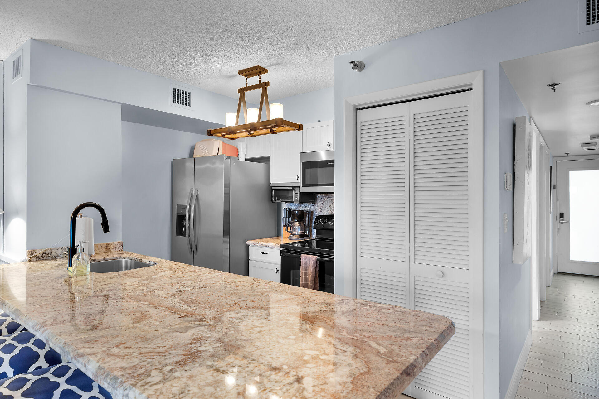 Kitchen with a large granite peninsula, stainless steel appliances, and white louvered pantry doors.