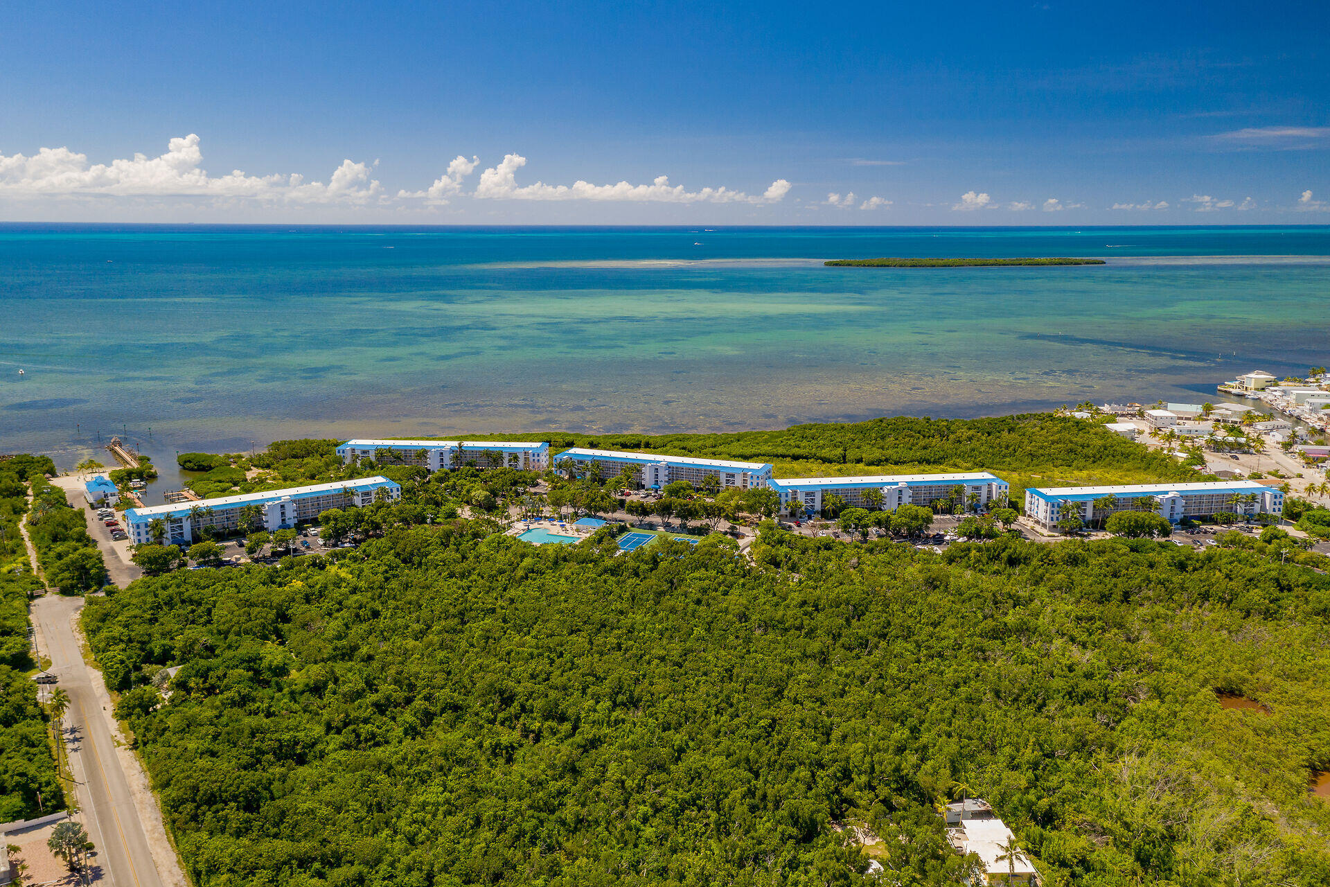 Waterfront condominium buildings bordered by mangroves, with ocean, pool, and tennis courts.