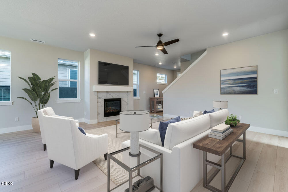 Staged living room with white seating and a marble fireplace beneath a mounted television.