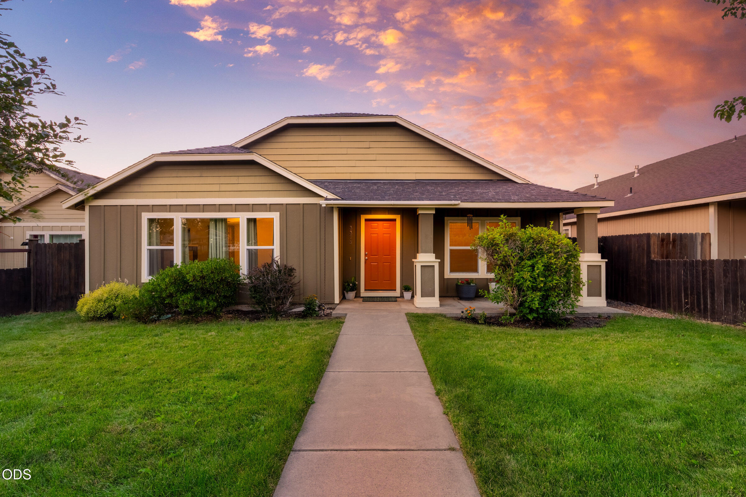Single-story tan home with an orange front door and walkway at sunset.