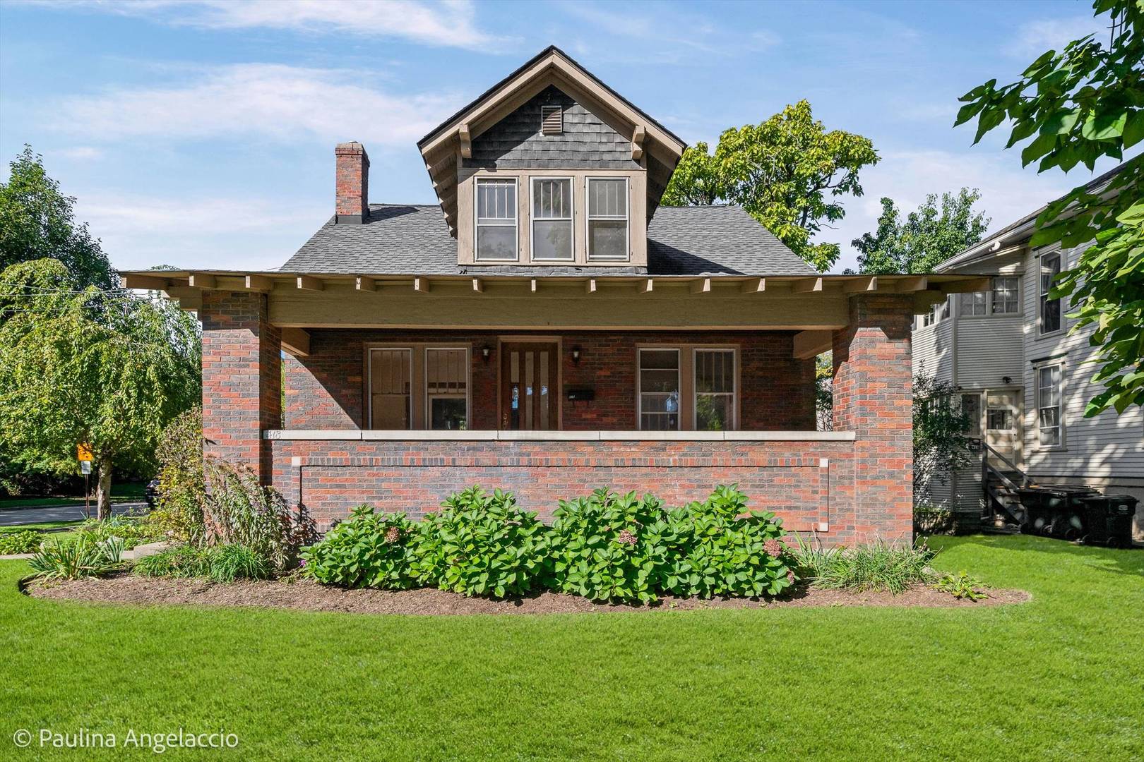 Brick house with a broad covered porch, upper dormer, and landscaped front lawn.