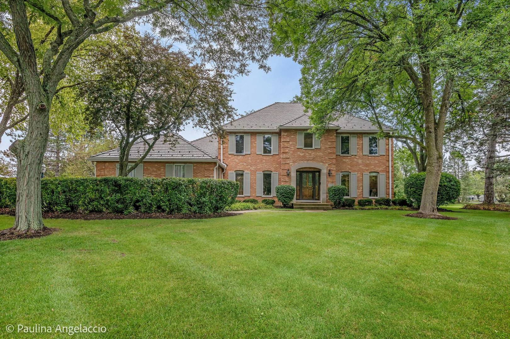 Two-story brick home with an arched entrance, framed by mature trees and a broad lawn.