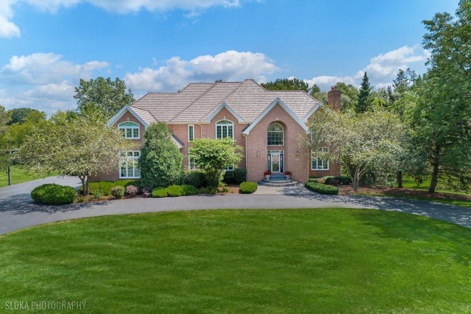 Large brick home with a tiled roof, landscaped front yard, and curved driveway.
